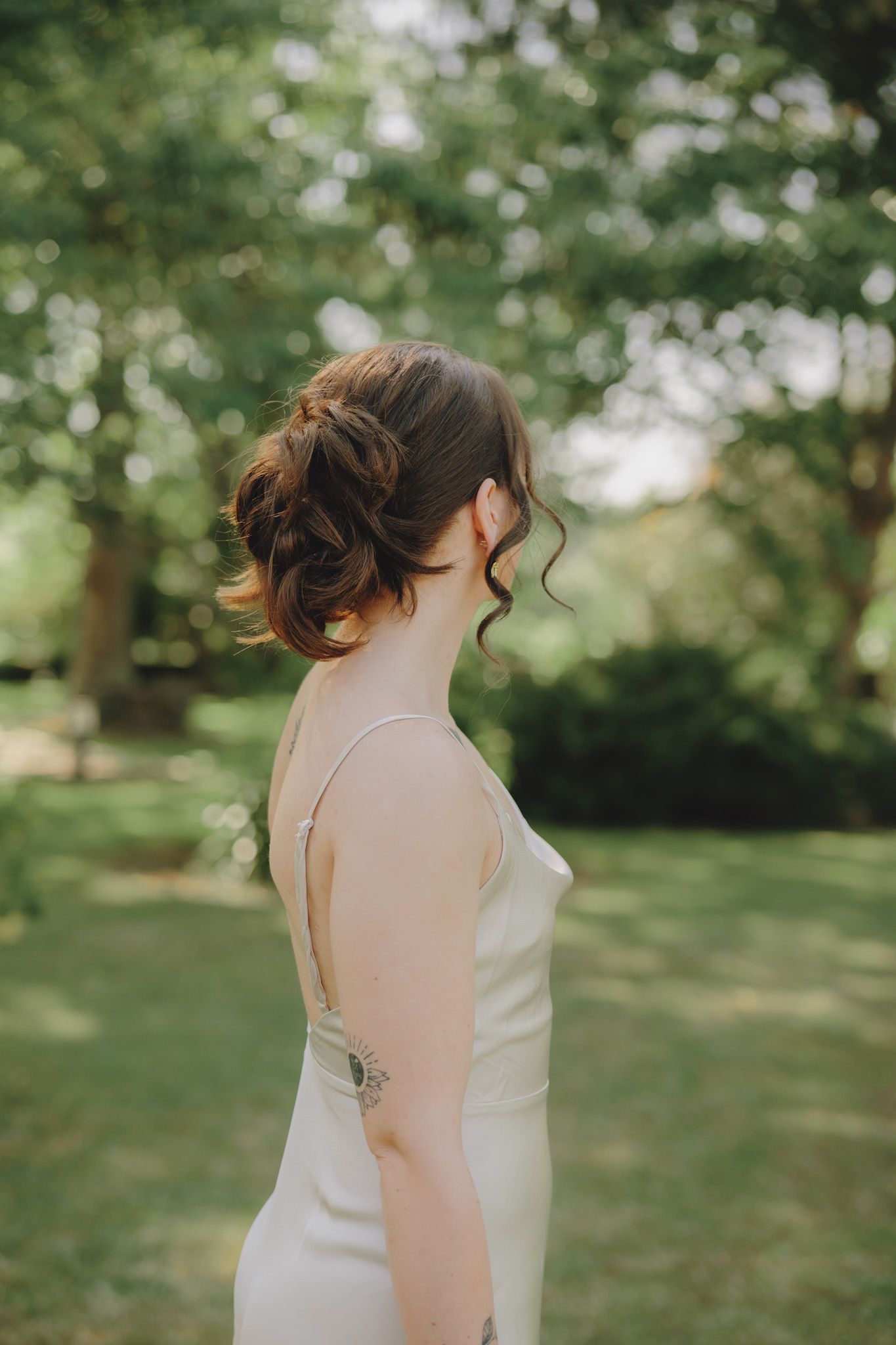 Side profile of elegant updo hairstyle with soft curls against natural garden background.
