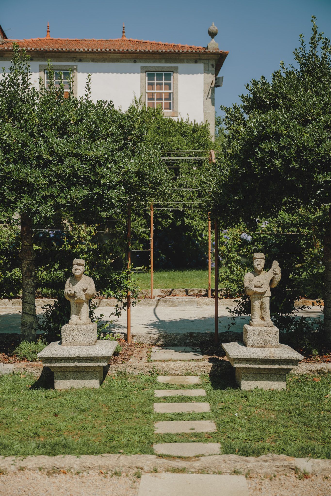 Row of stone sculptures displayed in a garden with white buildings in background.