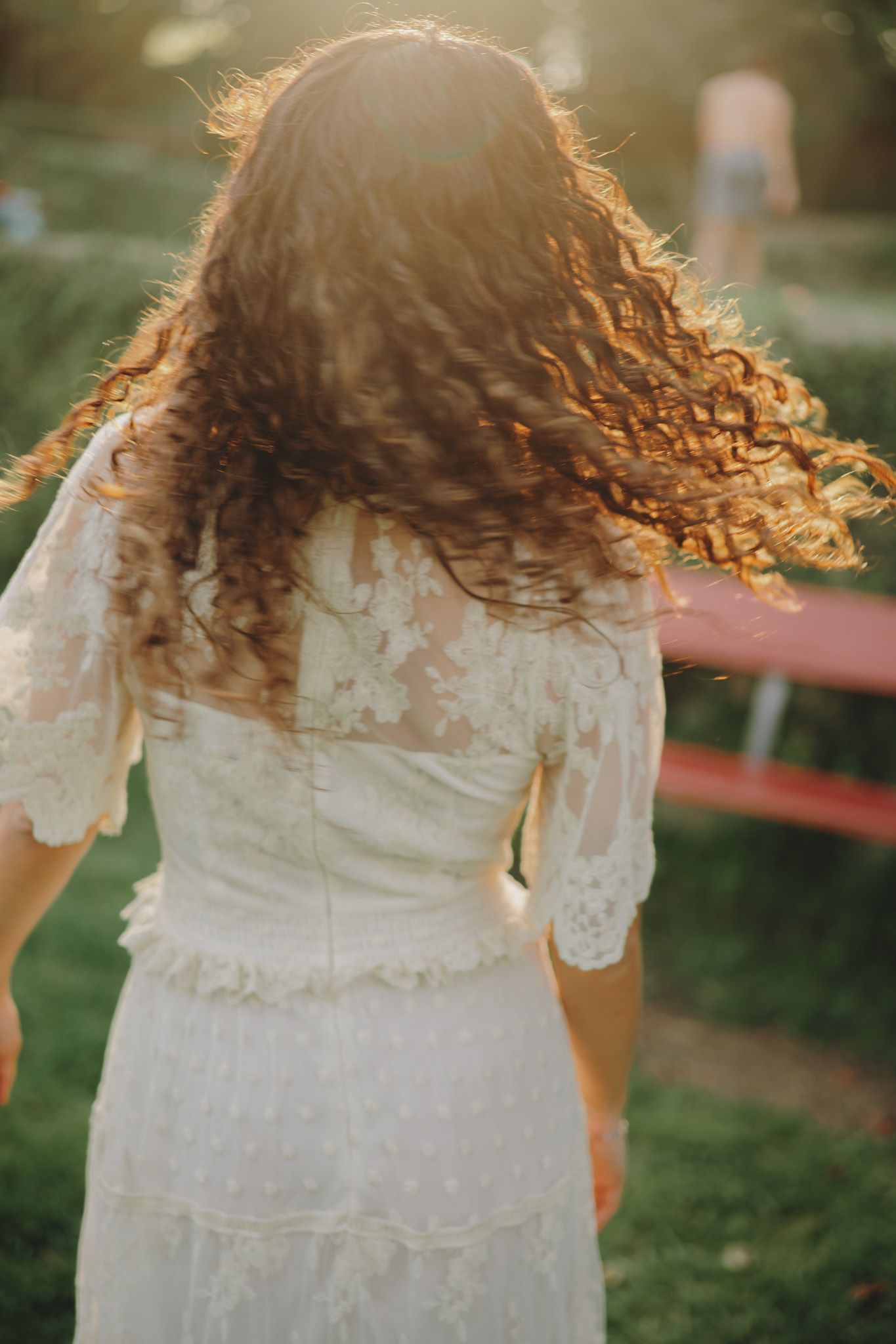 Flowing white lace dress and curly hair captured in ethereal garden lighting.