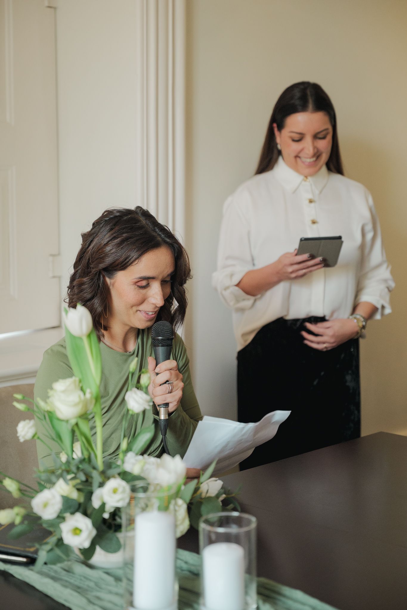 White floral arrangements in vases on a dark table during wedding preparations.