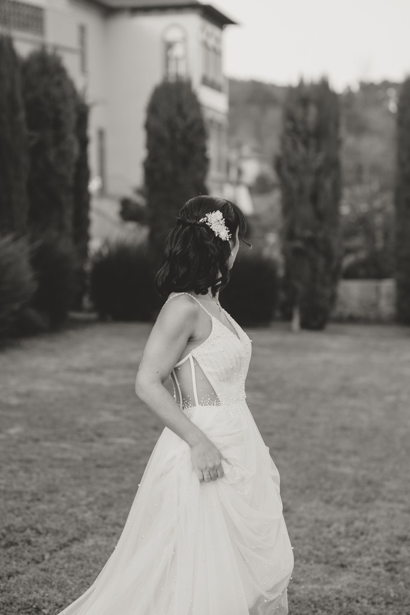 A bride in a white dress spins playfully in an outdoor garden setting.