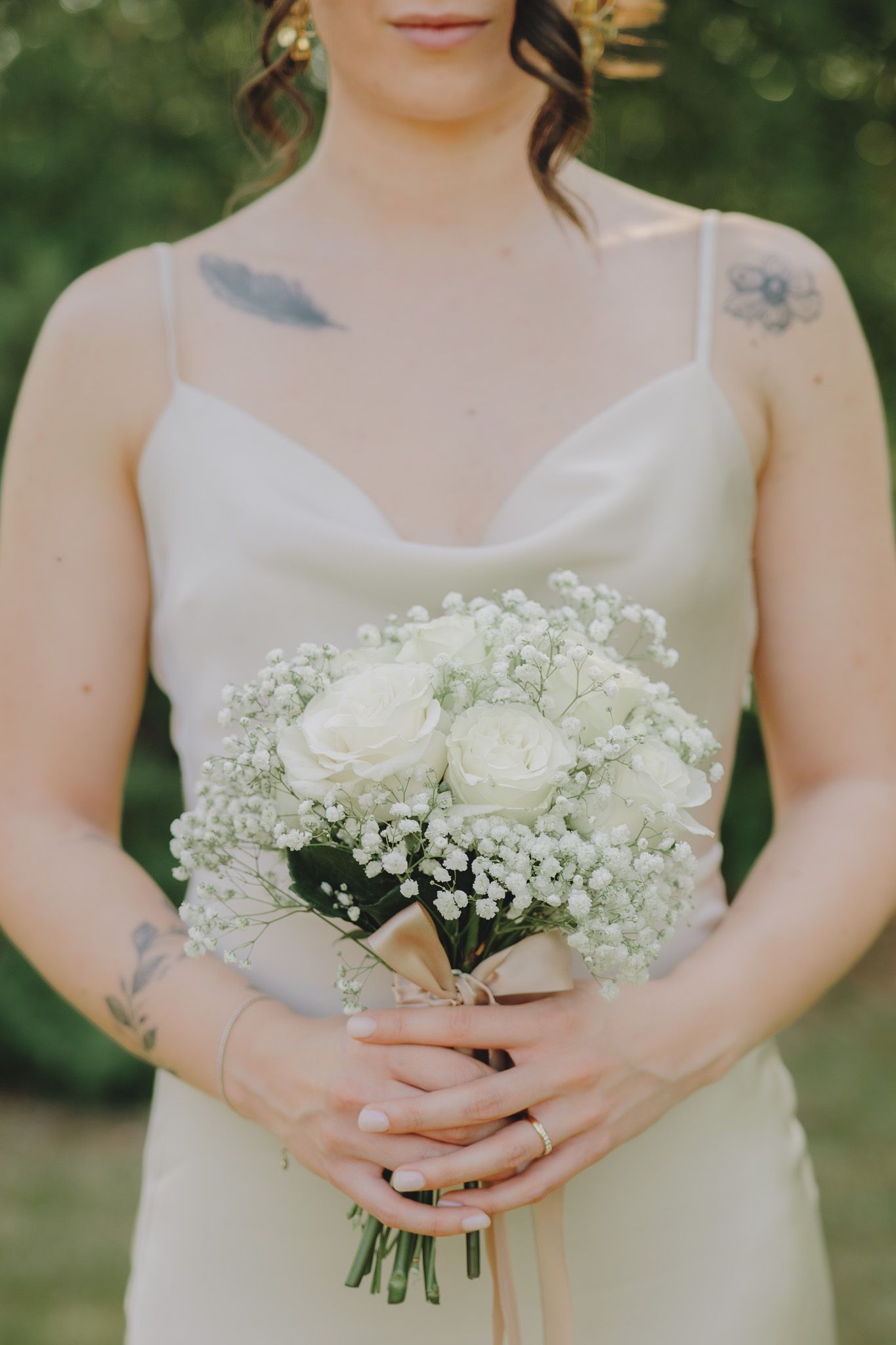 Delicate white and baby's breath bouquet held by hands wearing minimal jewelry against white dress.