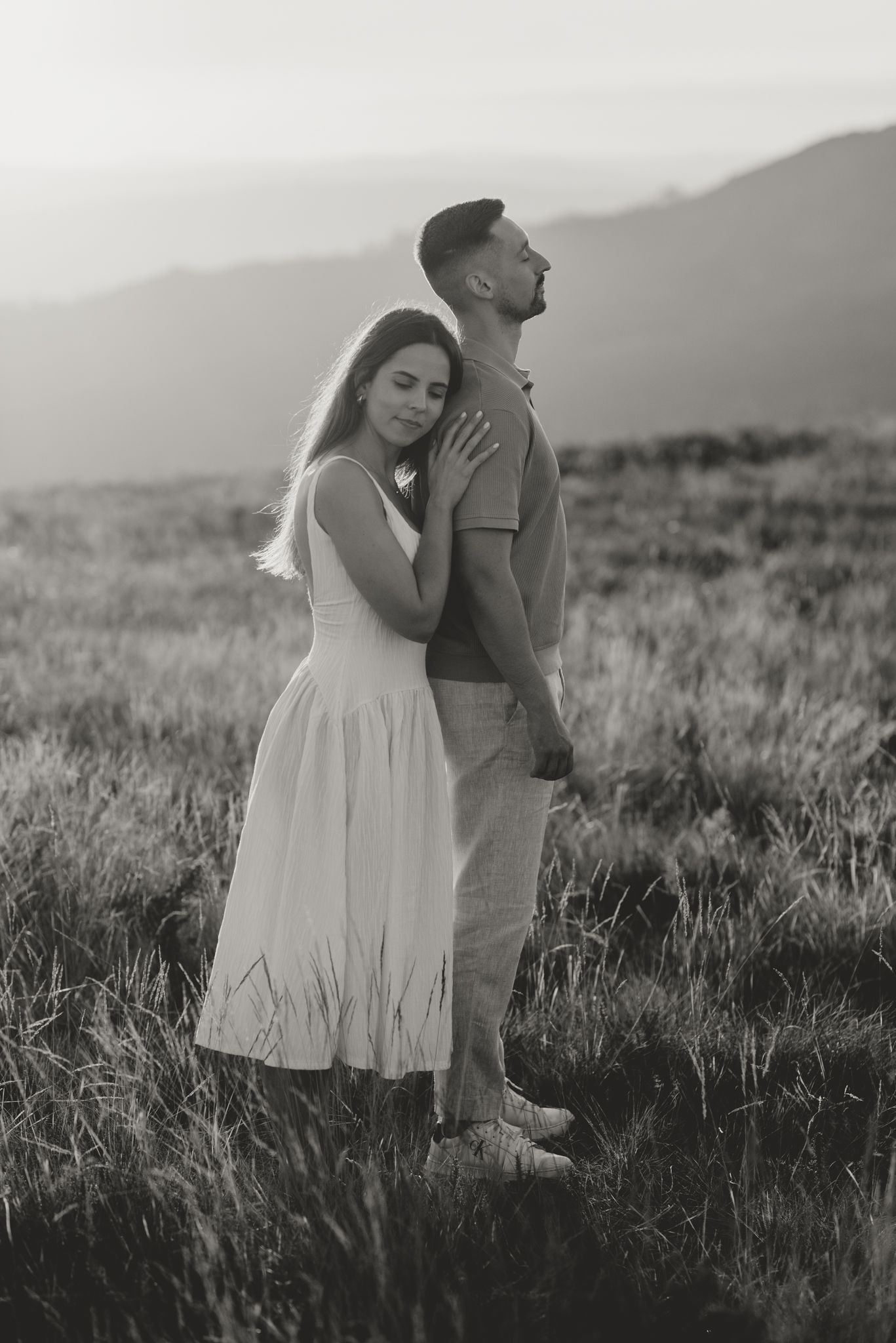 A romantic black and white photo of a couple in a grassy field at dusk.