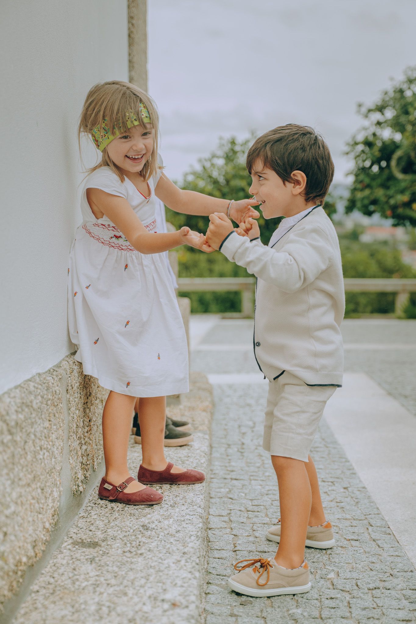 Children in white clothing playing and interacting on stone pathway outdoors.