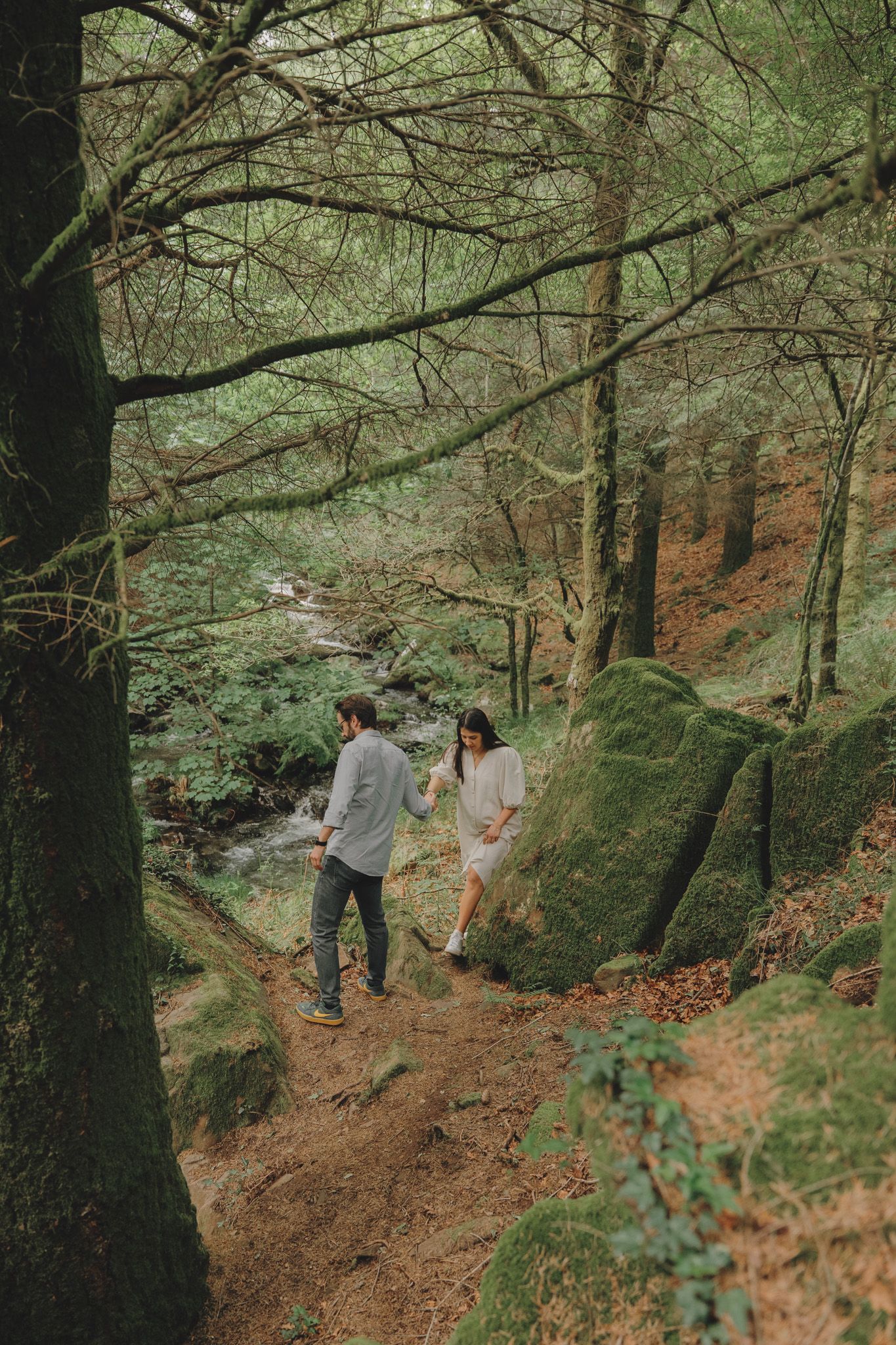 Couple walking together on a winding forest path near a stream.
