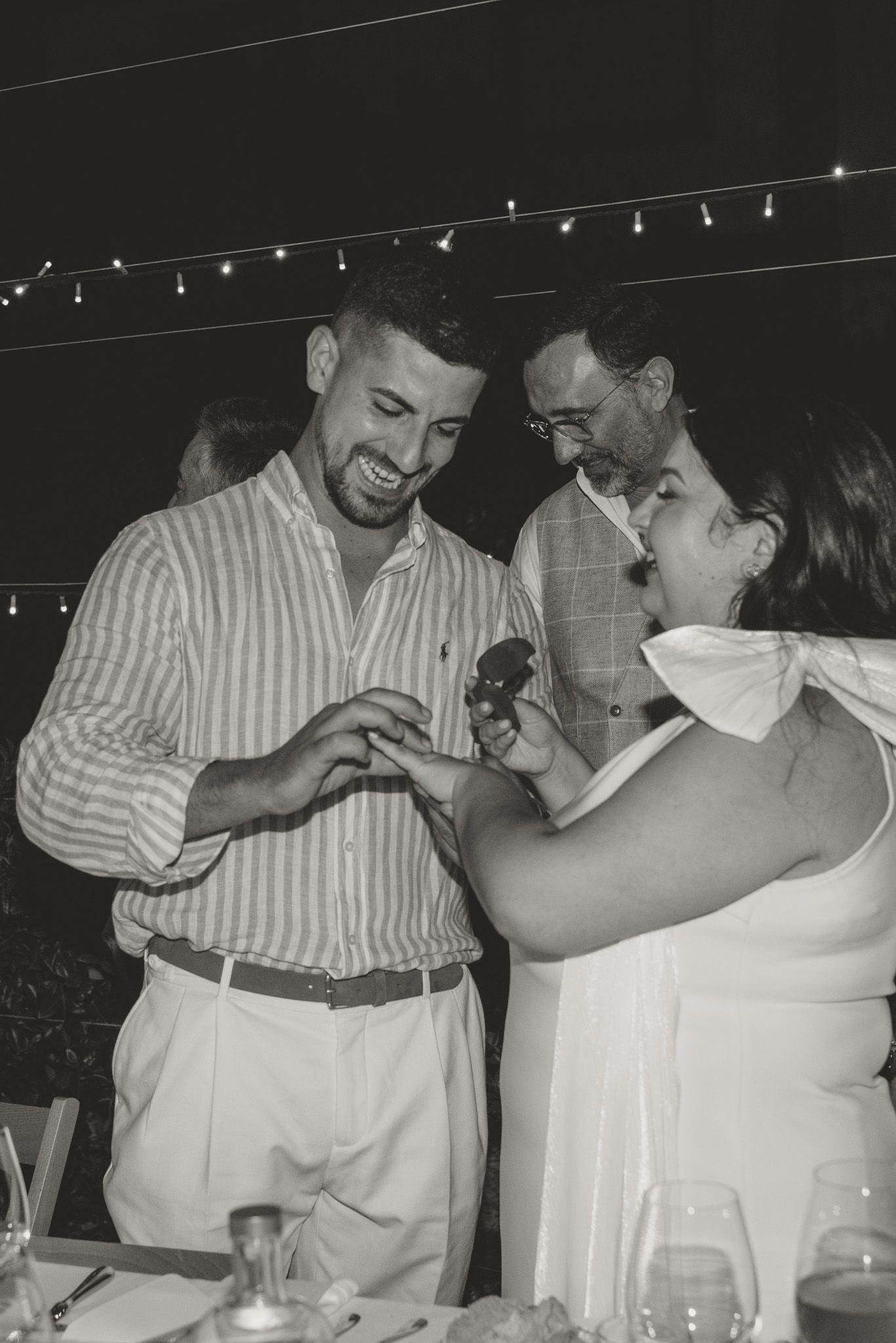 A joyful couple sharing laughter during their dinner celebration under string lights.
