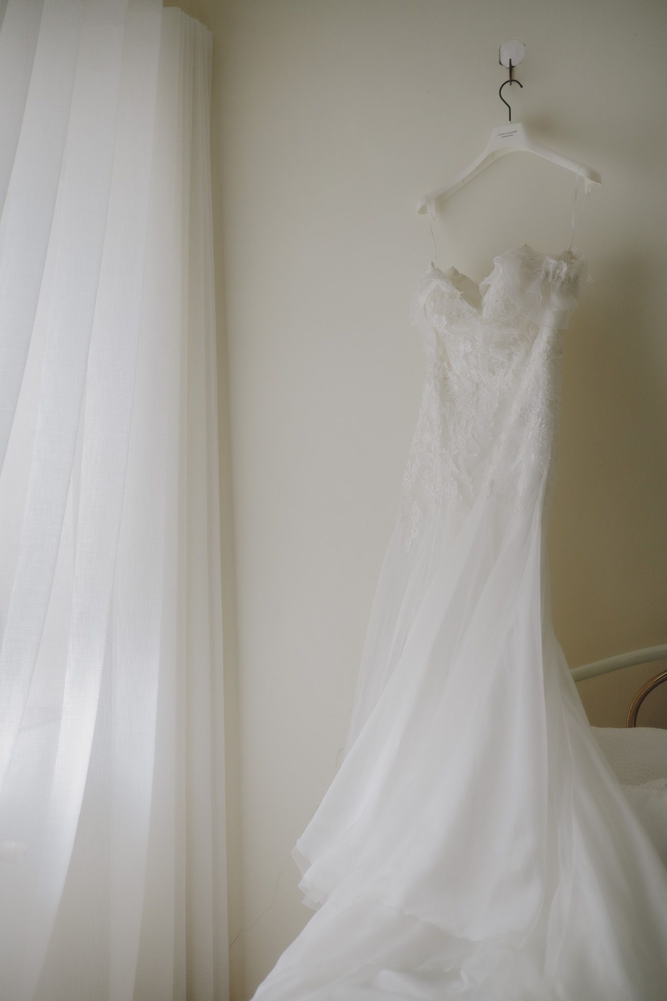 White wedding dress hanging against light wall with soft natural lighting.