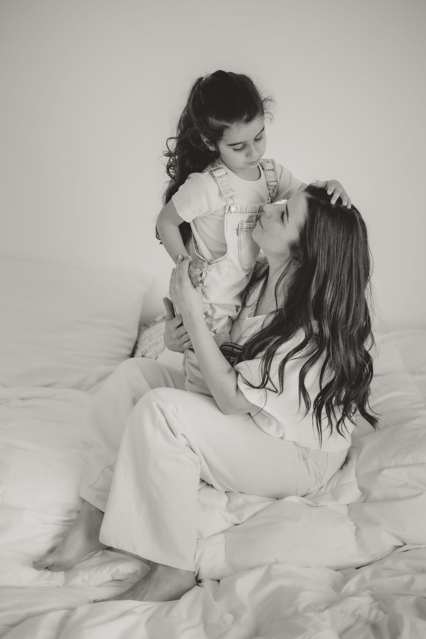 Black and white photo of a mother sitting on a bed, lovingly holding her young daughter close.