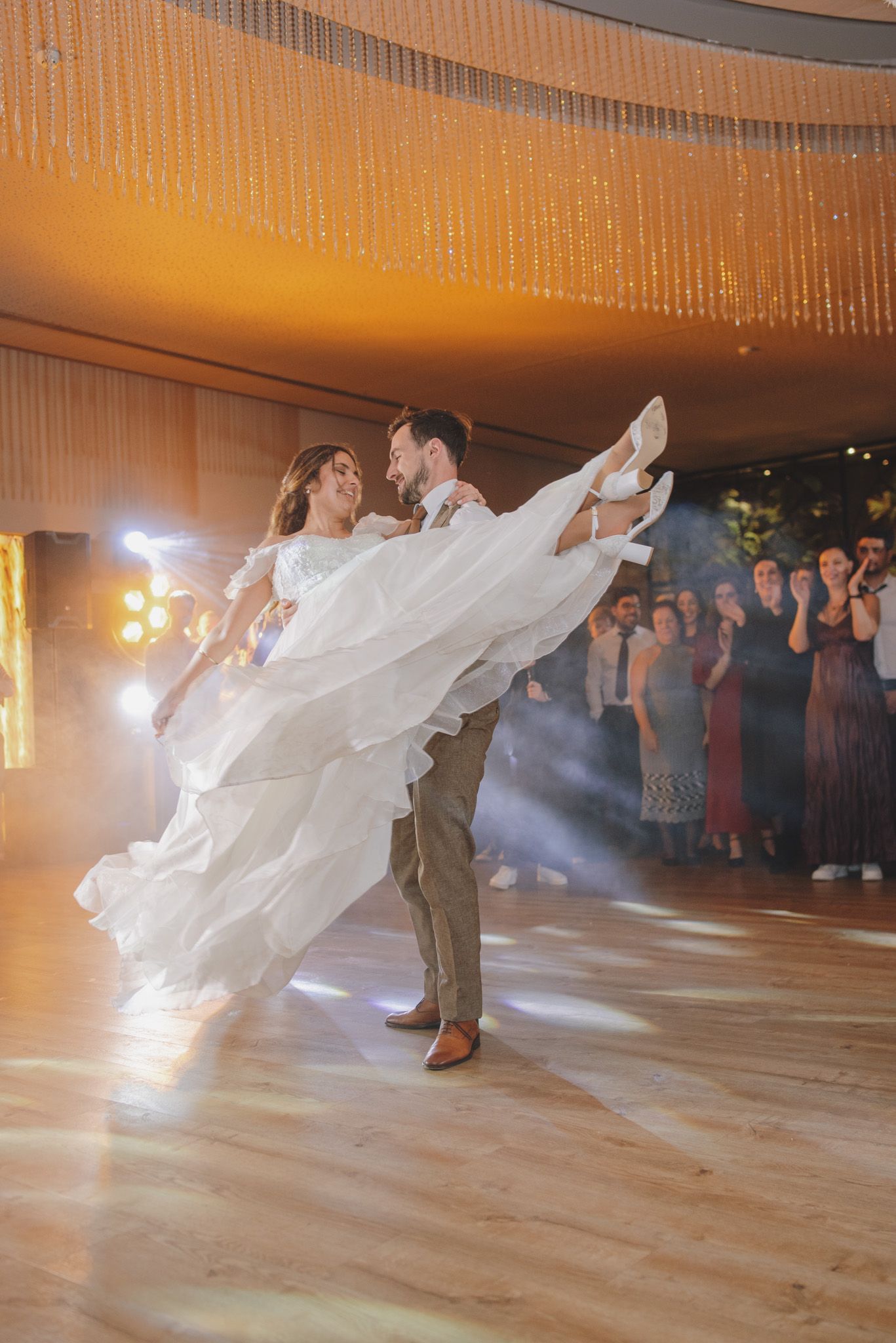Sequence of wedding dancers performing on wooden floor with flowing white dress and onlooking guests.