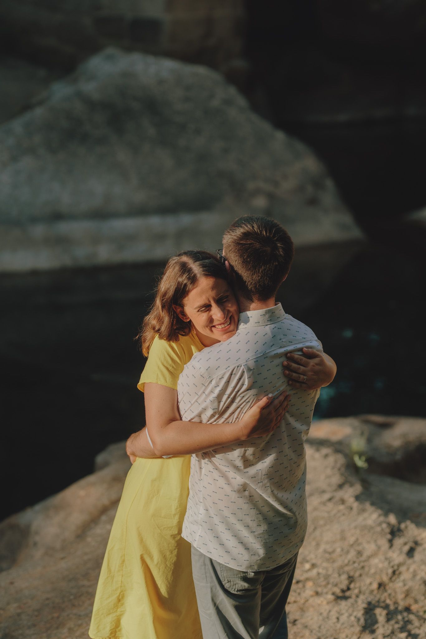 A couple embraces tenderly on a rocky outcrop during a romantic photoshoot.