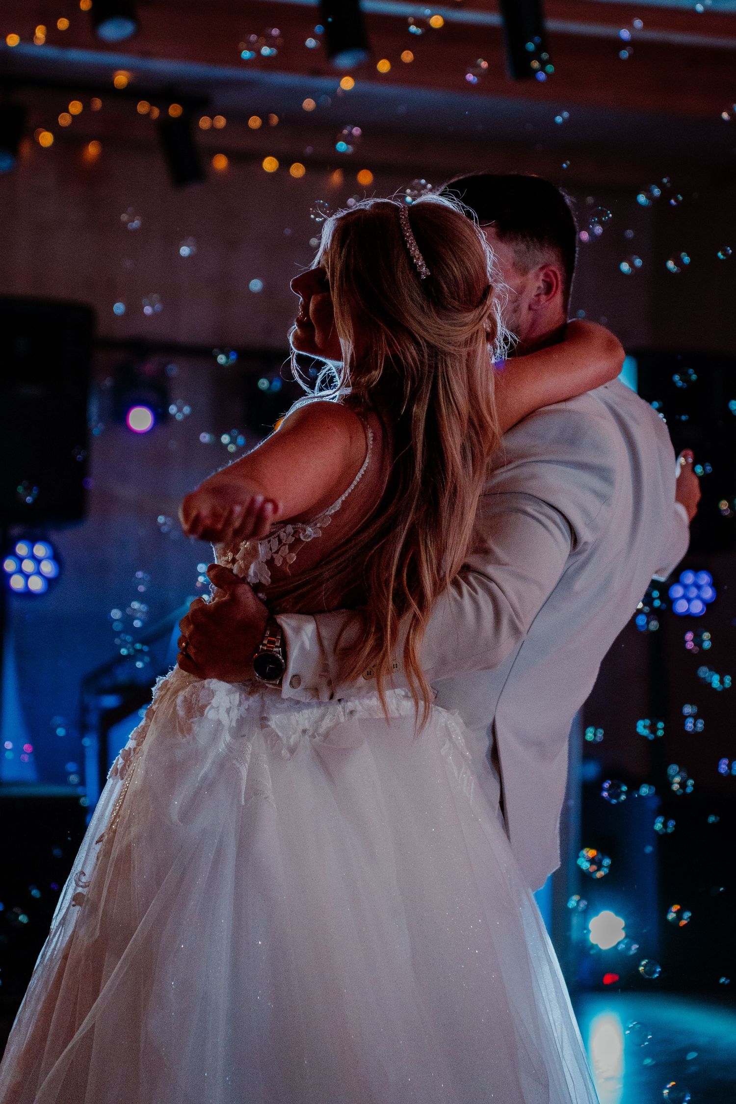 Bride and groom share their first dance surrounded by bubbles and colorful lights at a romantic wedding reception.