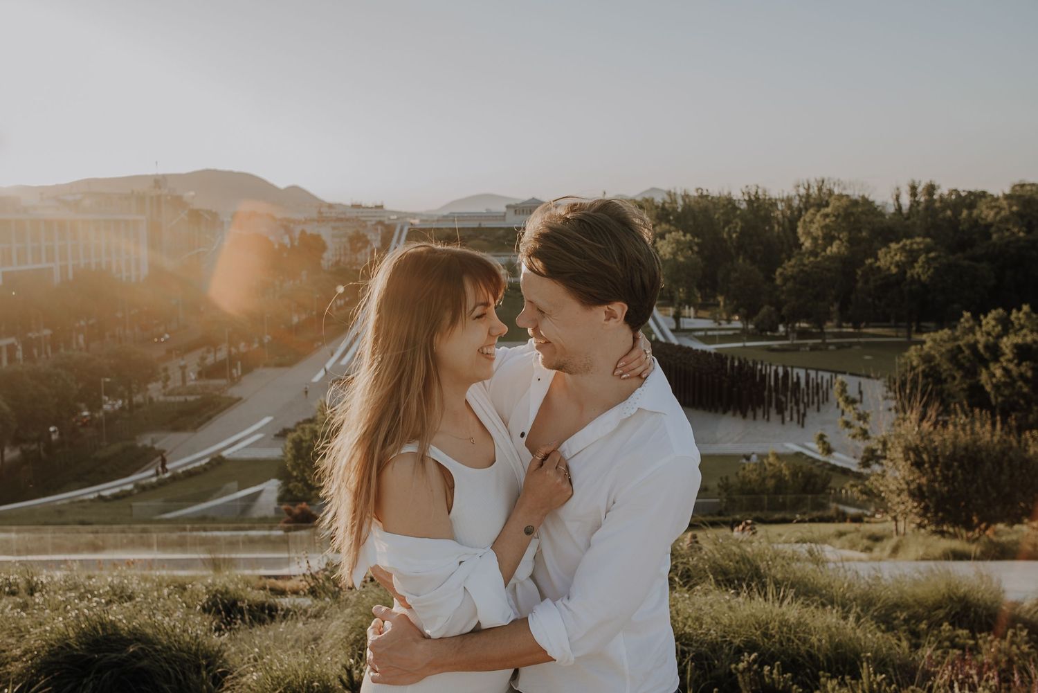 A golden sunset illuminates a romantic couple embracing on a hilltop overlooking a serene lake.