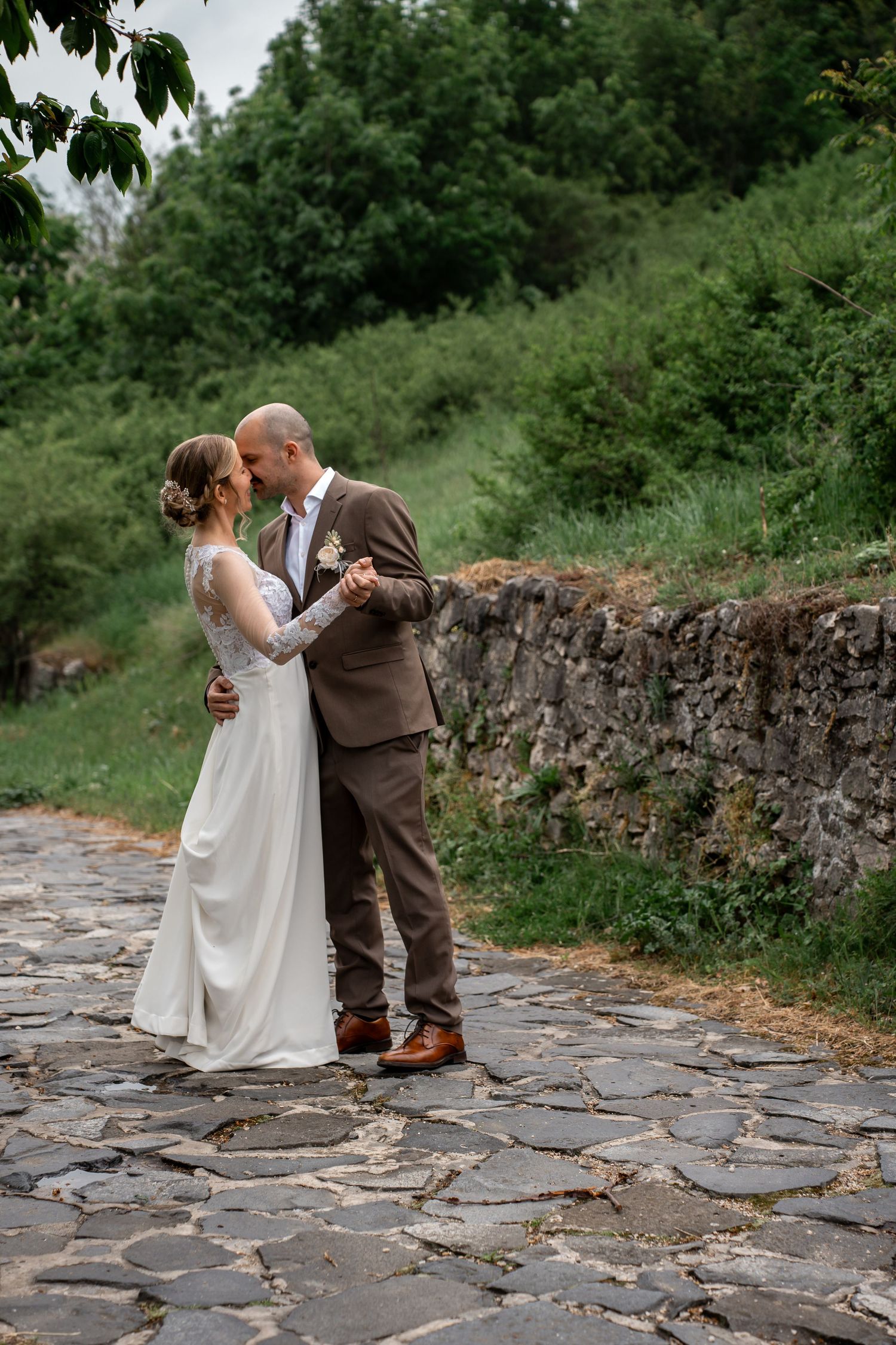 A romantic wedding couple embraces on a rustic stone pathway surrounded by lush greenery on their special day.