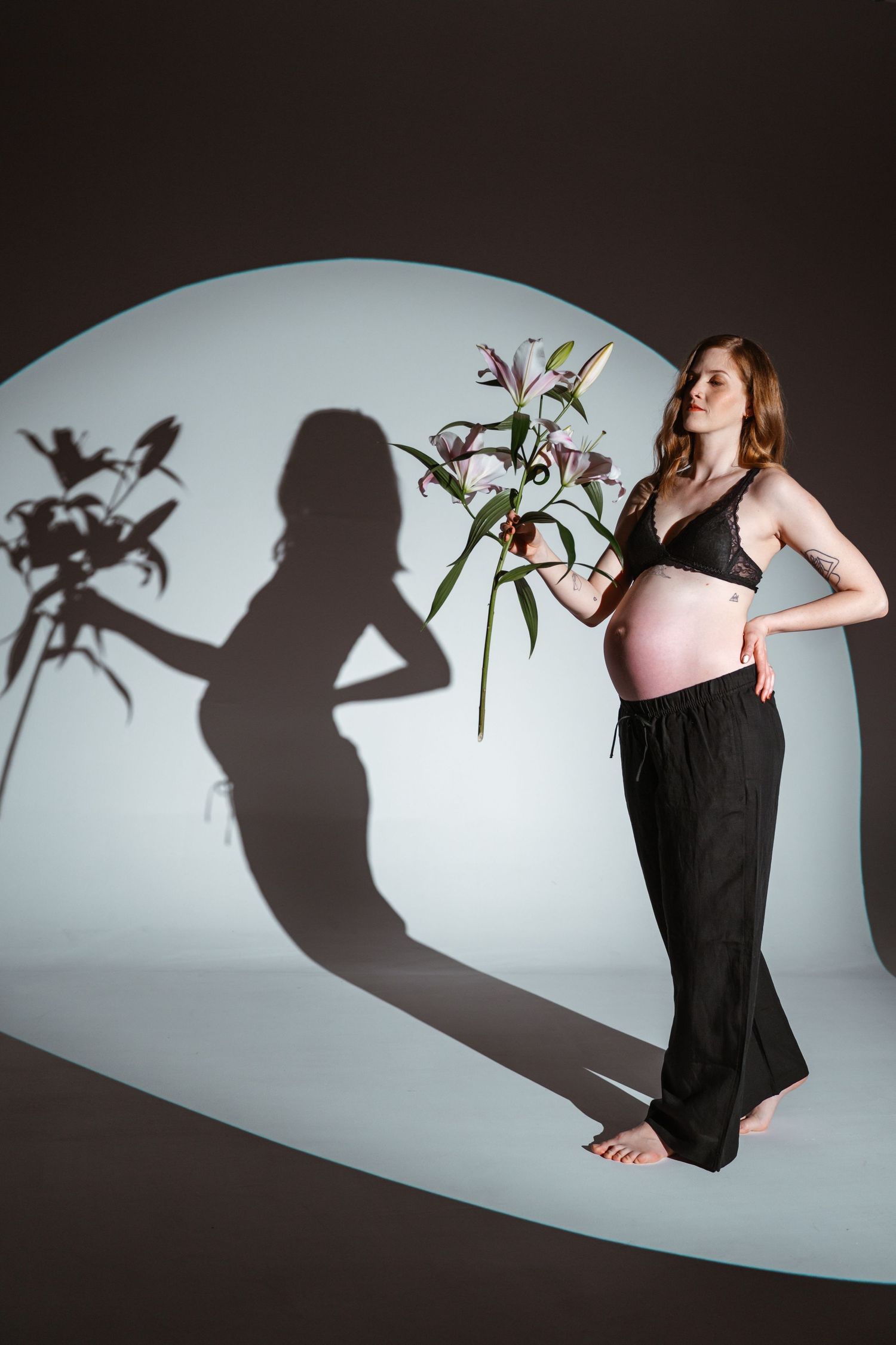 Artistic maternity photo with shadow play featuring an expectant mother posing with flowers against a circular backdrop.