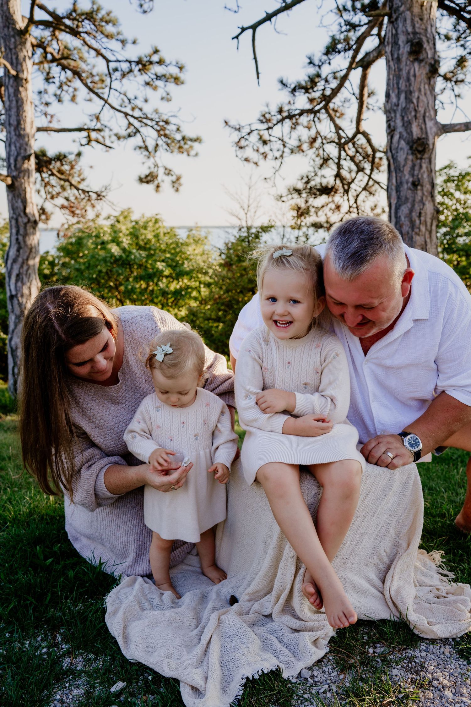 A family wearing white clothing shares joyful moments together while sitting outdoors in nature during golden hour.