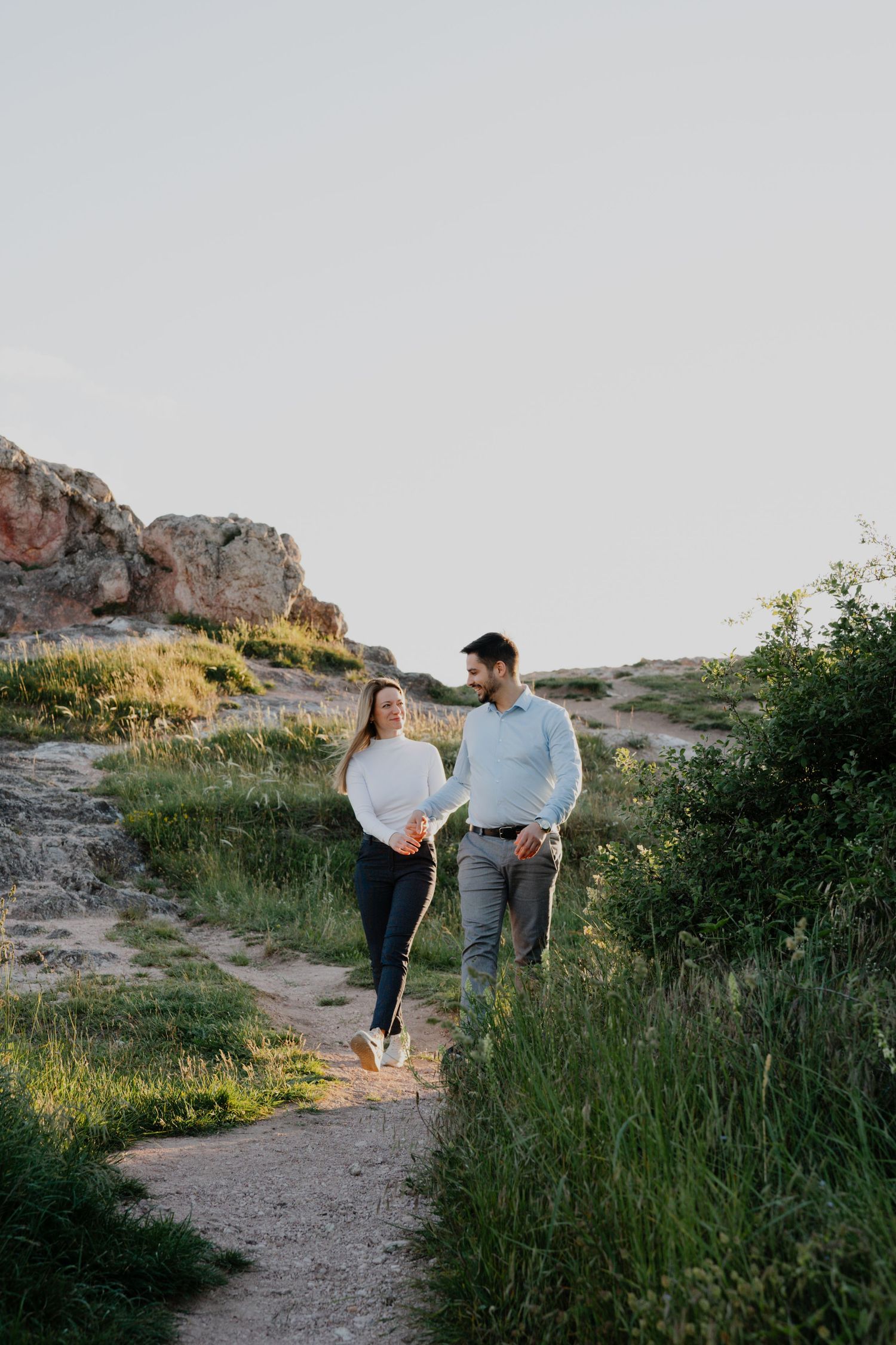 Couple walking together on a beautiful rocky mountain trail at sunset amid desert scrub and wildflowers.