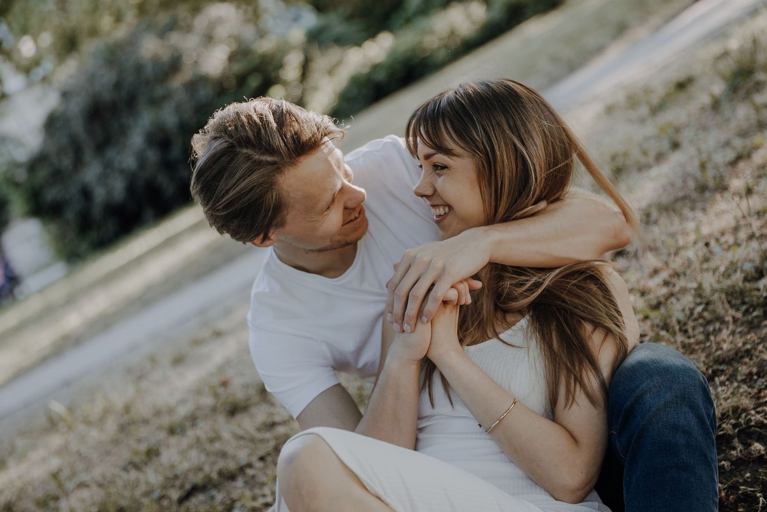 A young couple sits together on grassy hillside sharing an intimate moment at sunset.