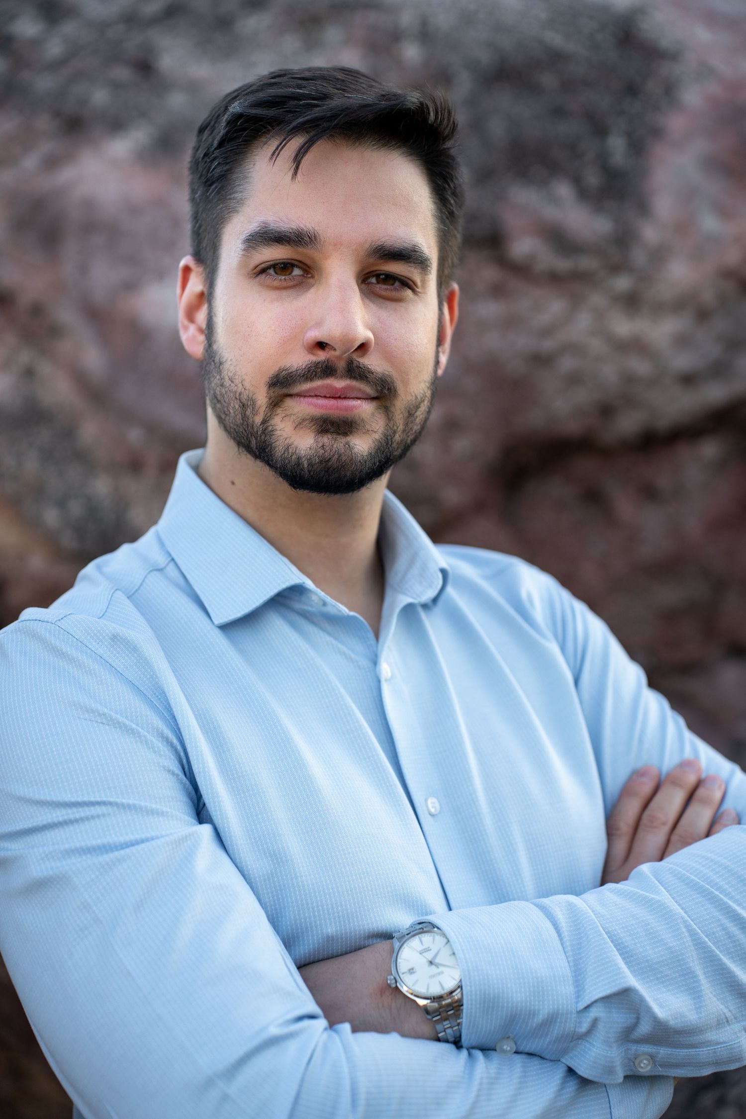 A person wearing a light blue dress shirt poses outdoors against a blurred background in a professional looking photo series.