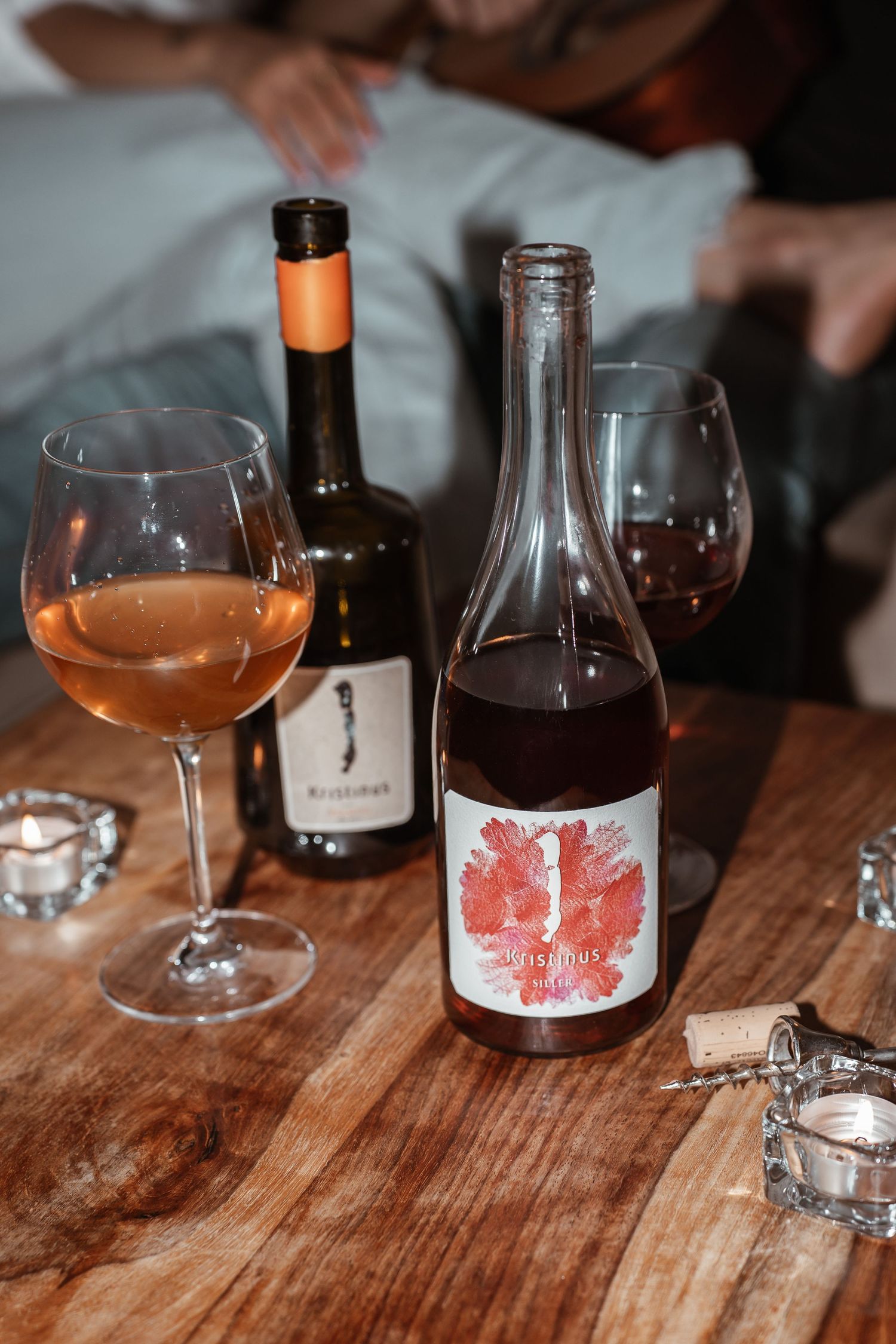 Wine bottles and glasses arranged on a rustic wooden table in warm lighting create an intimate tasting atmosphere.