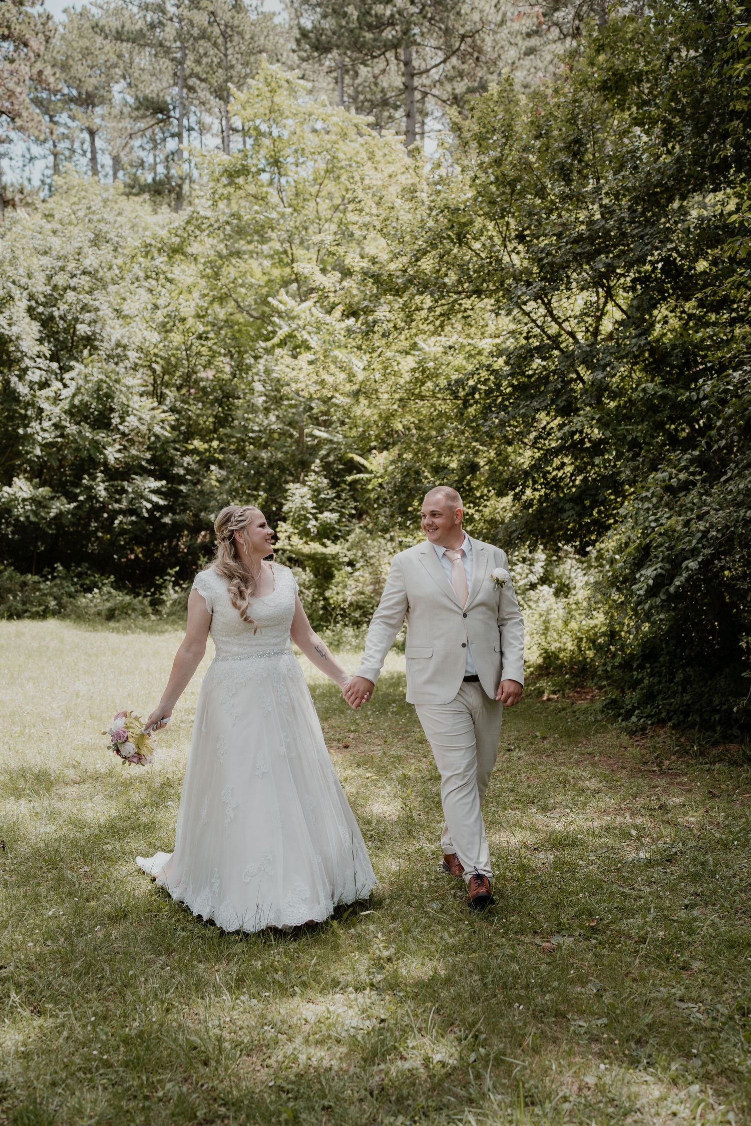A joyful bride and groom hold hands walking through a lush green garden on their wedding day.