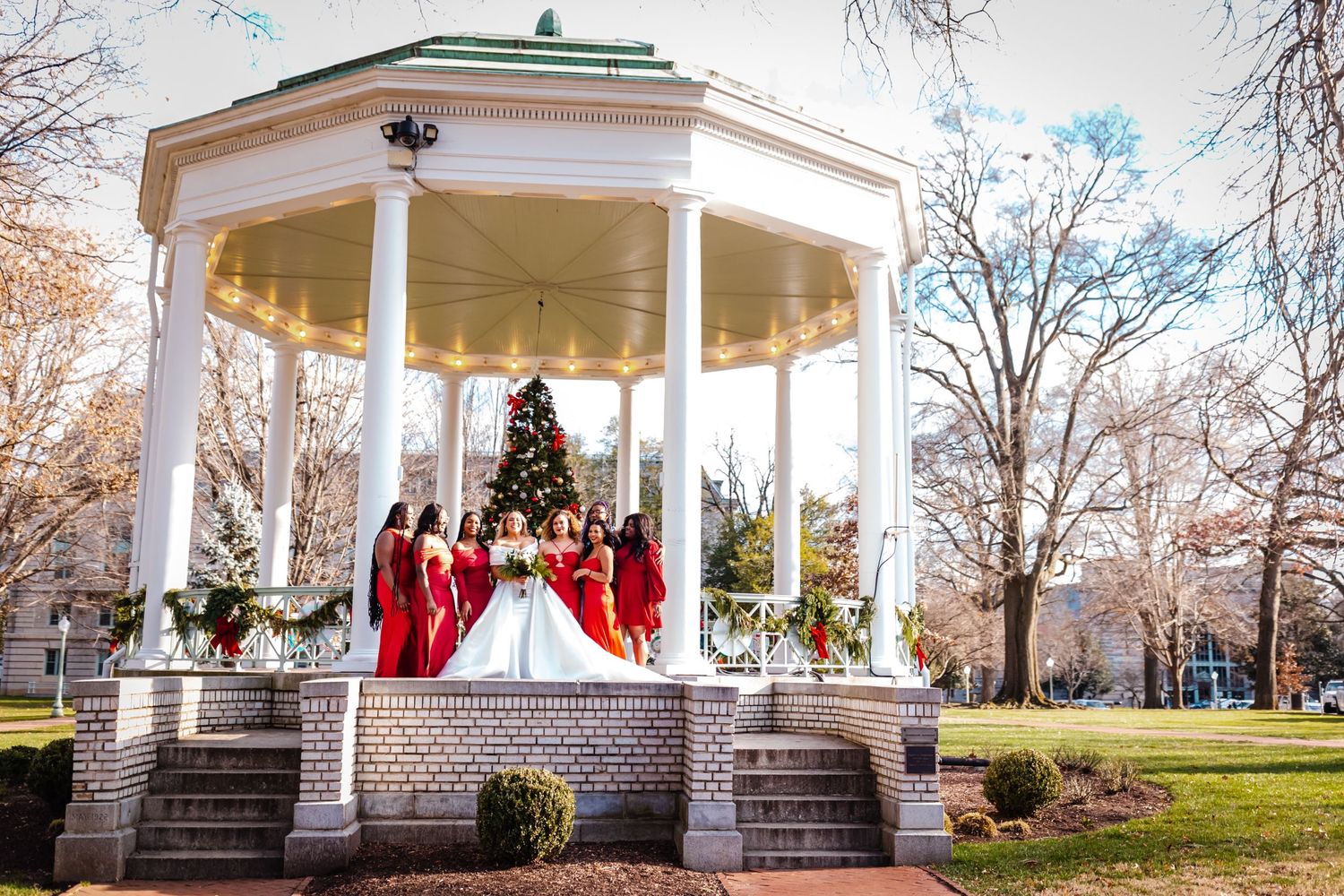 Christmas wedding ceremony at a white gazebo decorated with red accents and a Christmas tree.