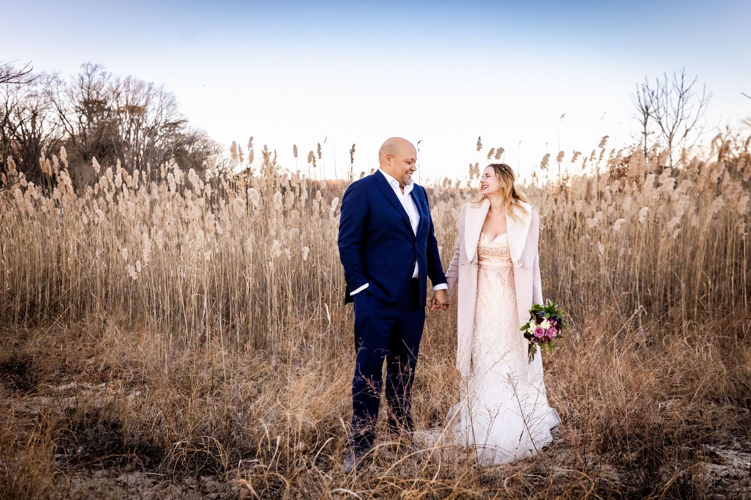 Wedding couple standing in tall golden grass during sunset.