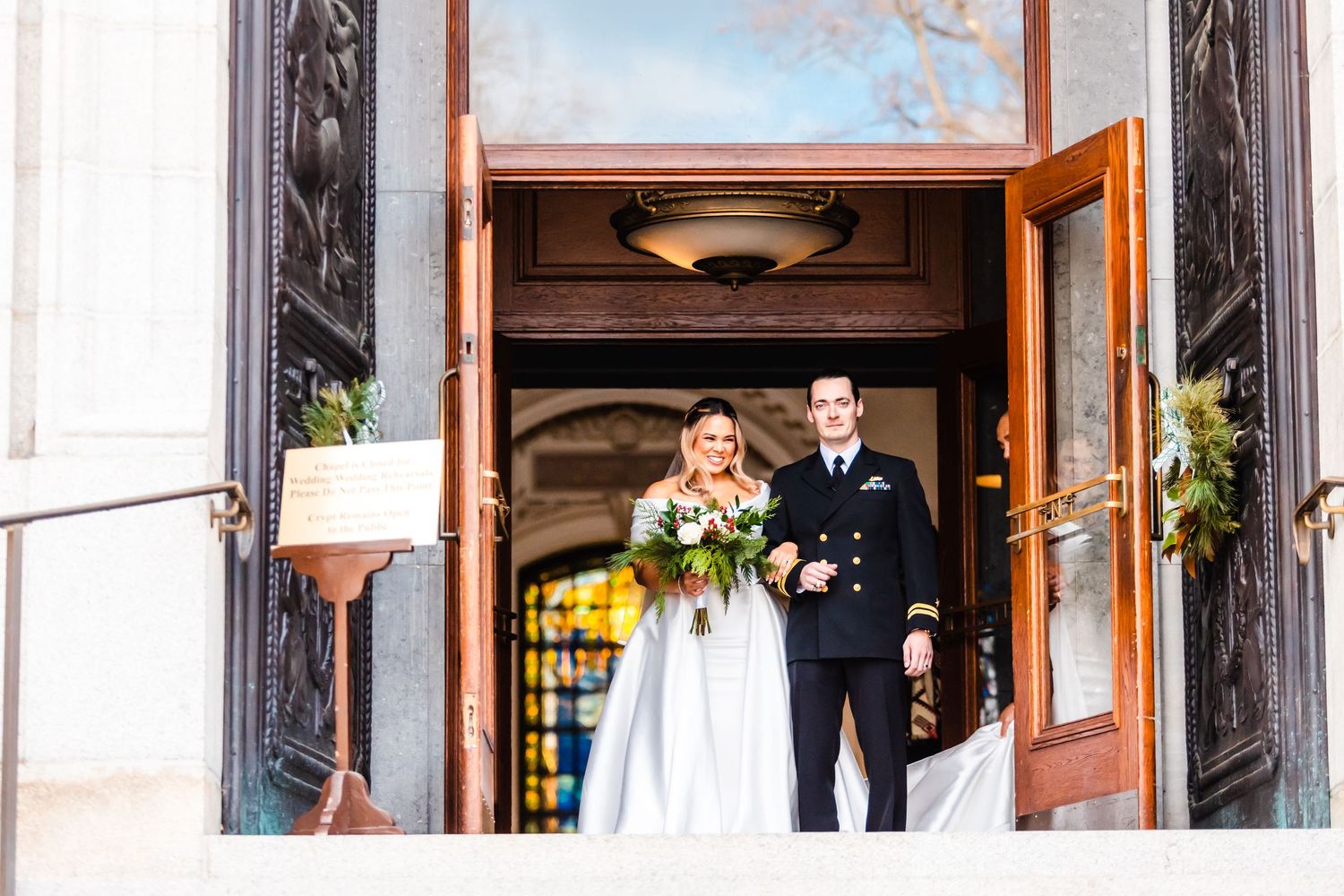 Wedding couple exiting ornate church doors with flowers and decor.