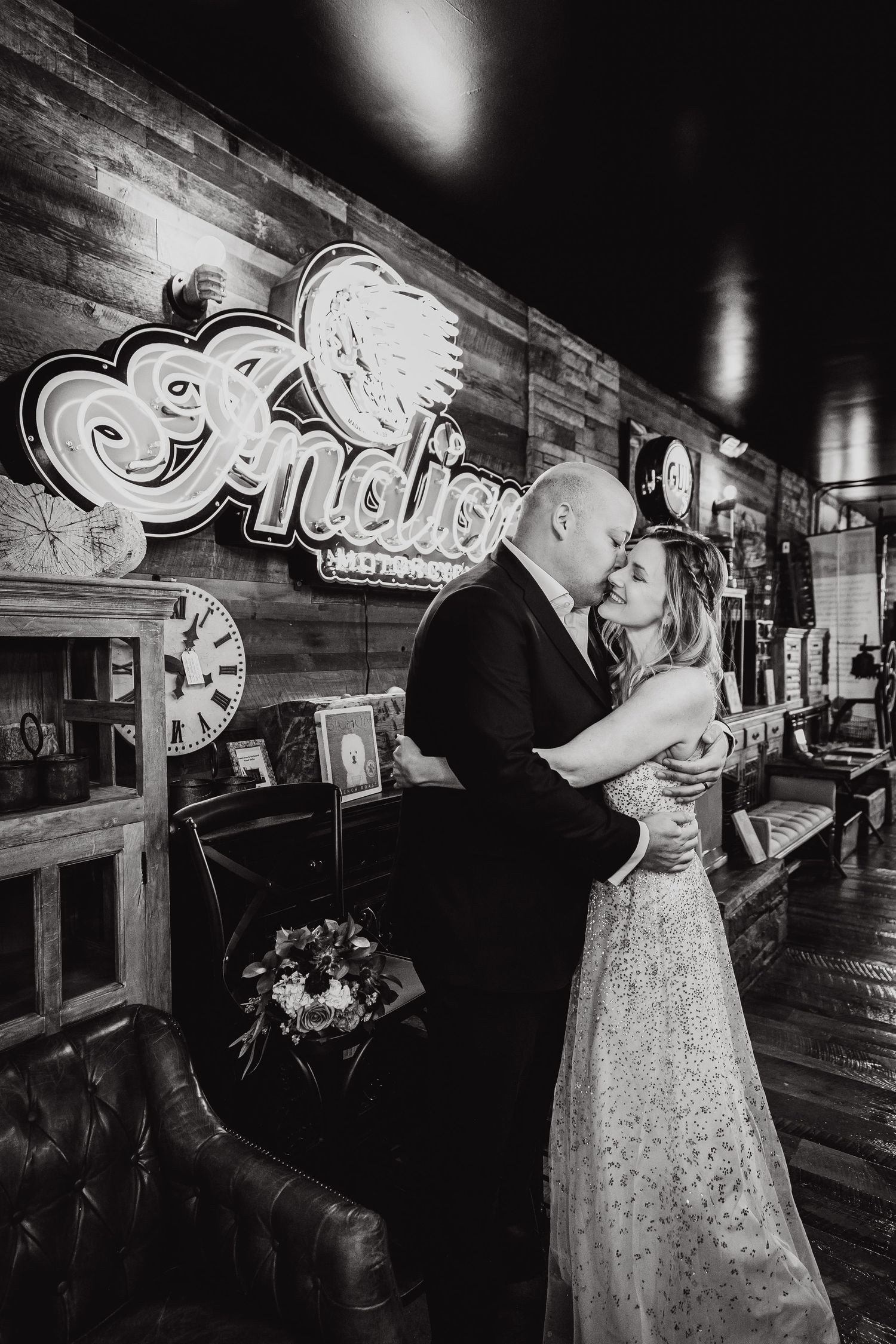A romantic black and white moment shared between newlyweds inside a rustic bar with vintage neon signage.
