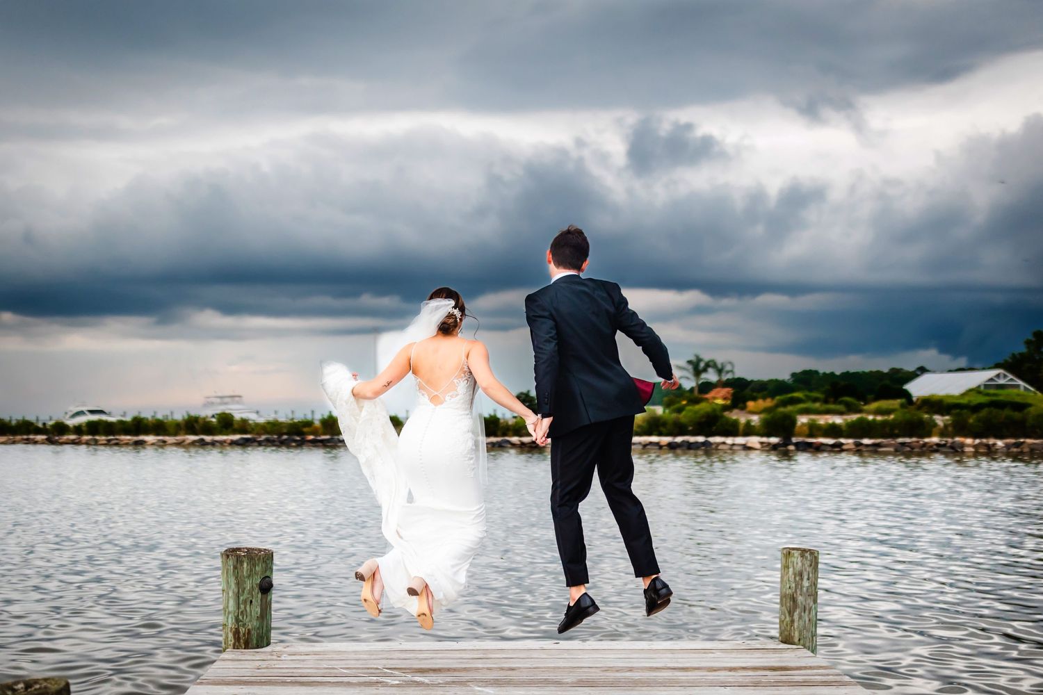 Couple jumps playfully on wooden dock with dramatic storm clouds in background.