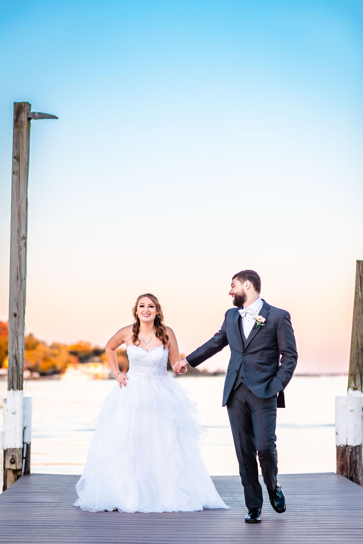 A couple walking hand in hand on a wooden pier during golden hour.