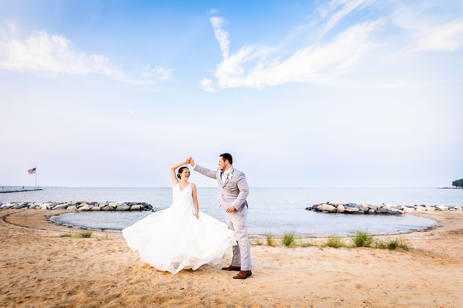 Wedding couple dancing on beach with white dress against blue ocean backdrop.
