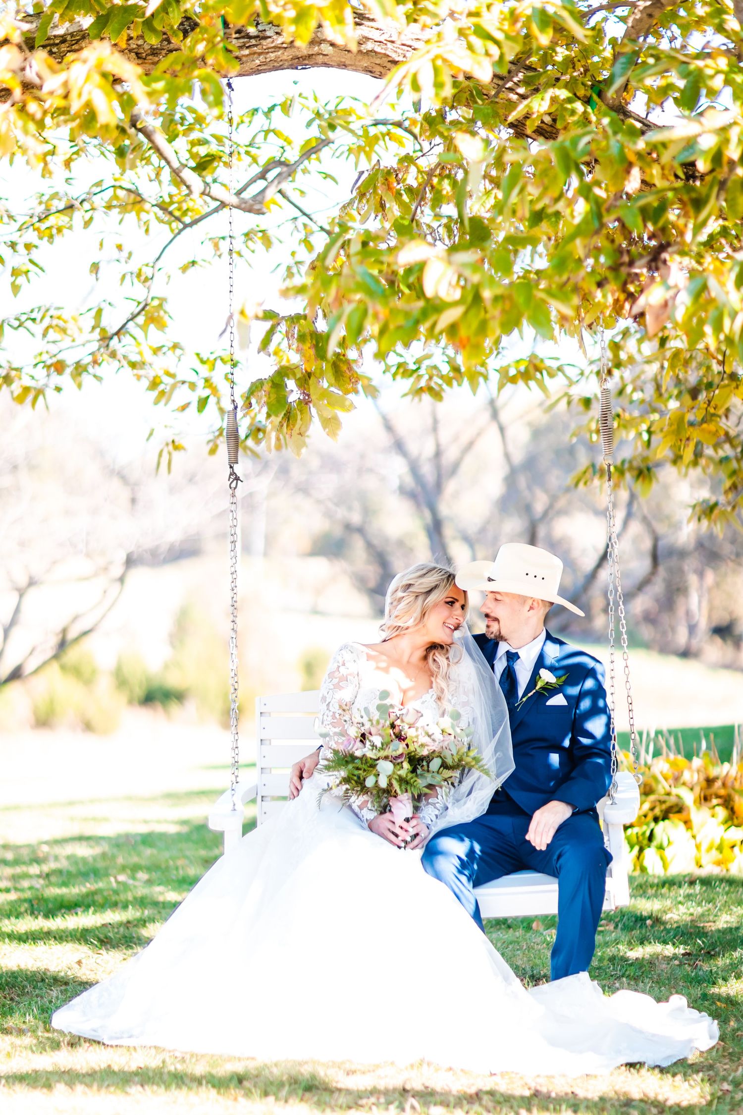 A dreamy autumn wedding scene with a couple sitting on a swing under golden leaves in soft sunlight.