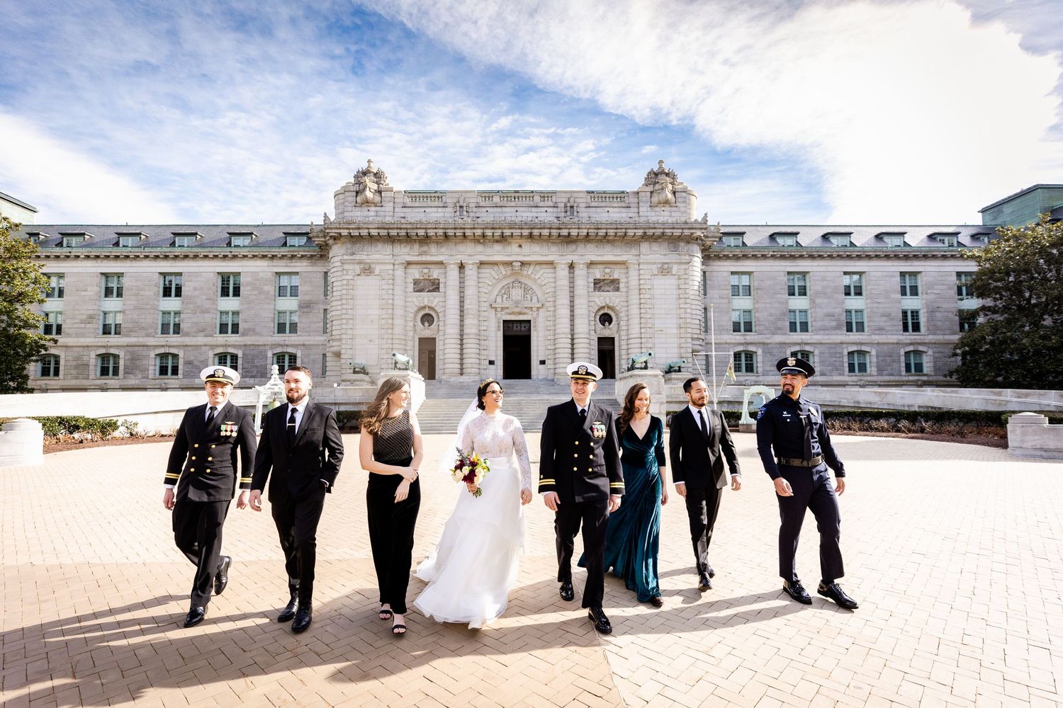 Wedding party walking together outside a grand historic building on a sunny day.