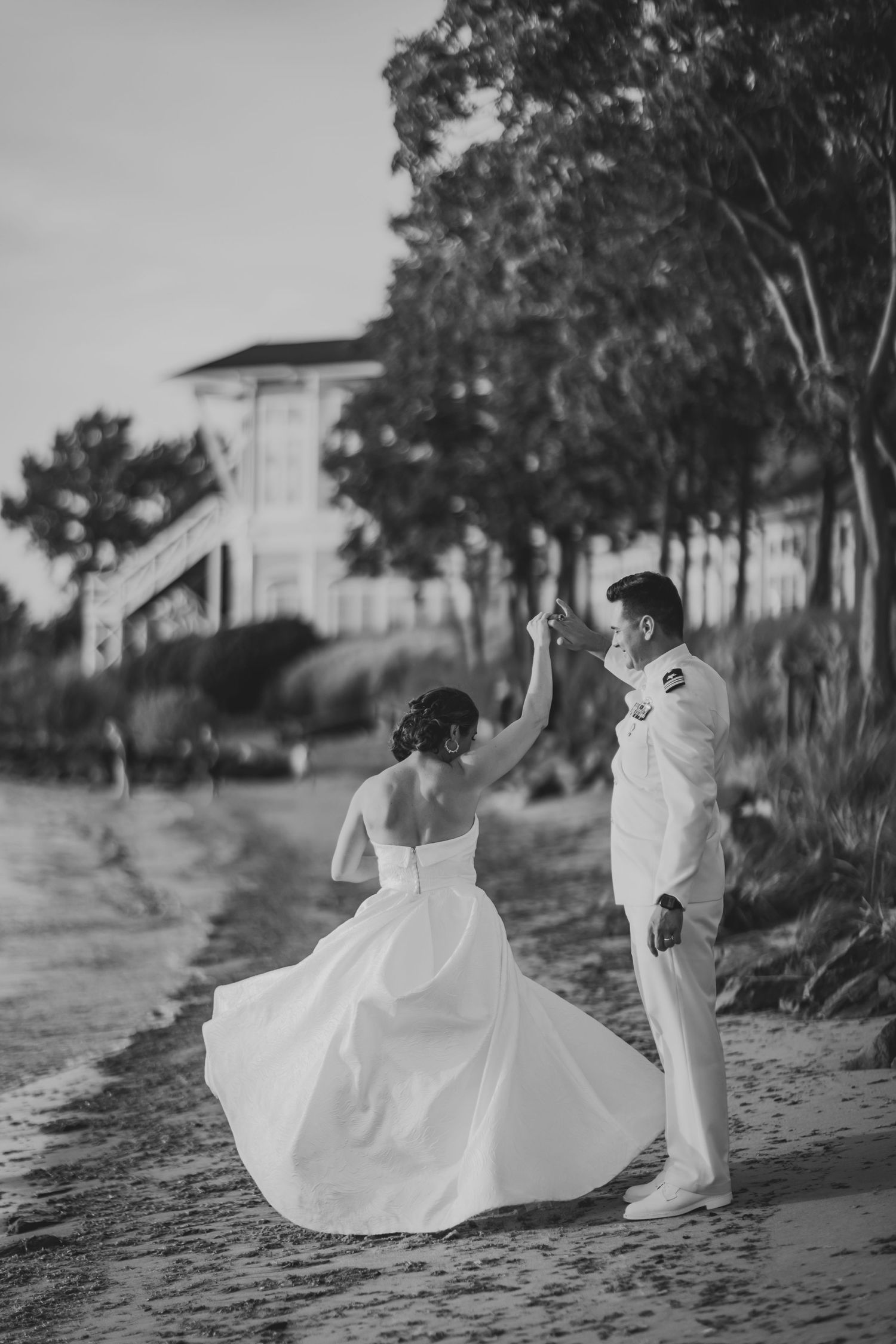 Black and white beach wedding photo with couple dancing on sandy path.