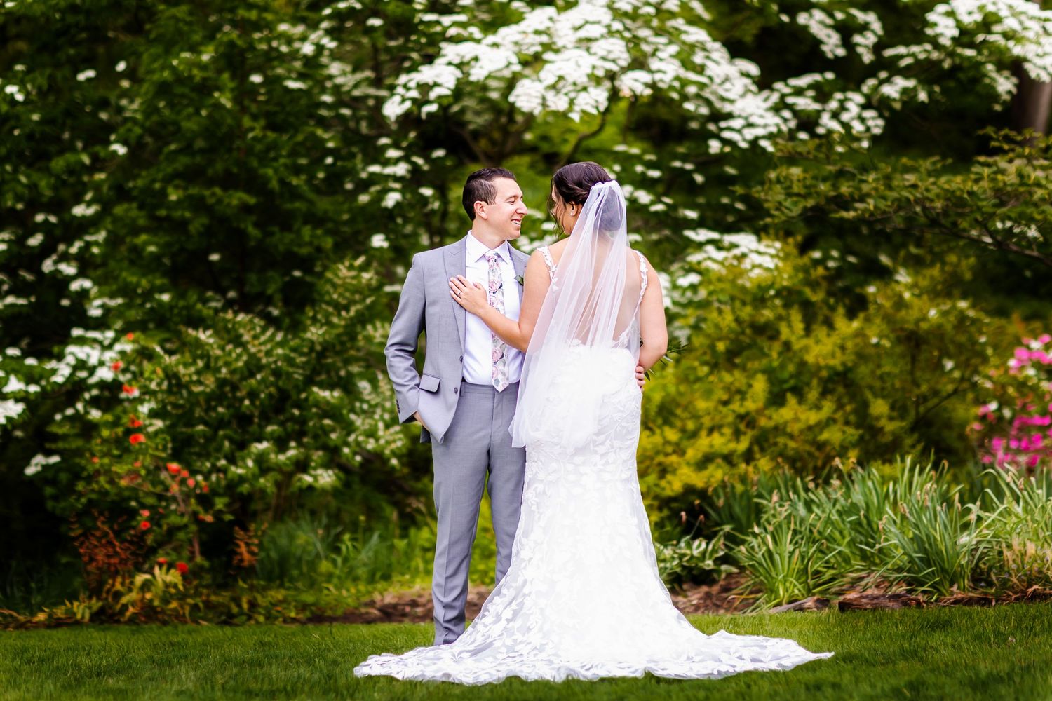 Garden wedding portrait with lush greenery and white flowering trees in background.