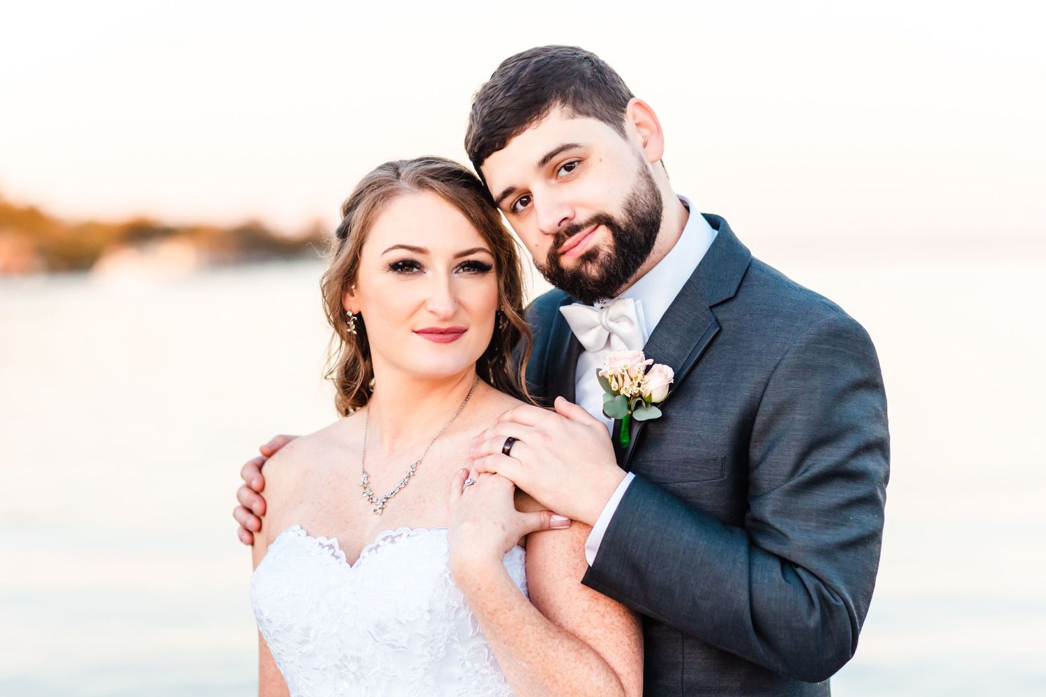 Close-up portrait of newlyweds embracing outdoors at sunset.