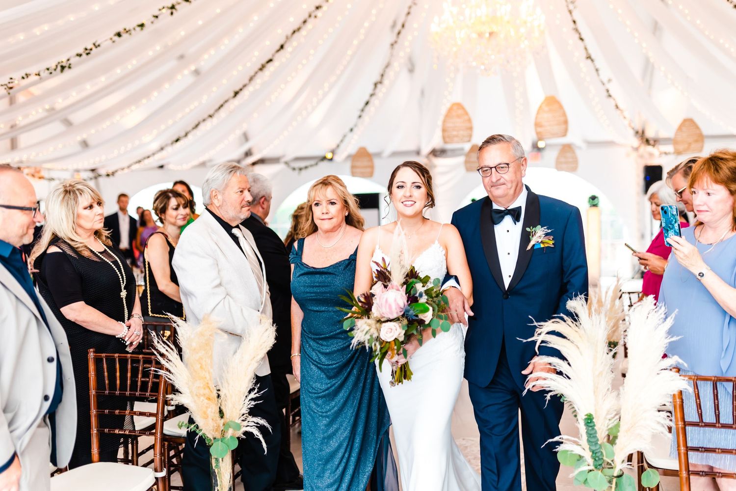 Wedding ceremony inside an elegant white tent decorated with draping and floral arrangements.