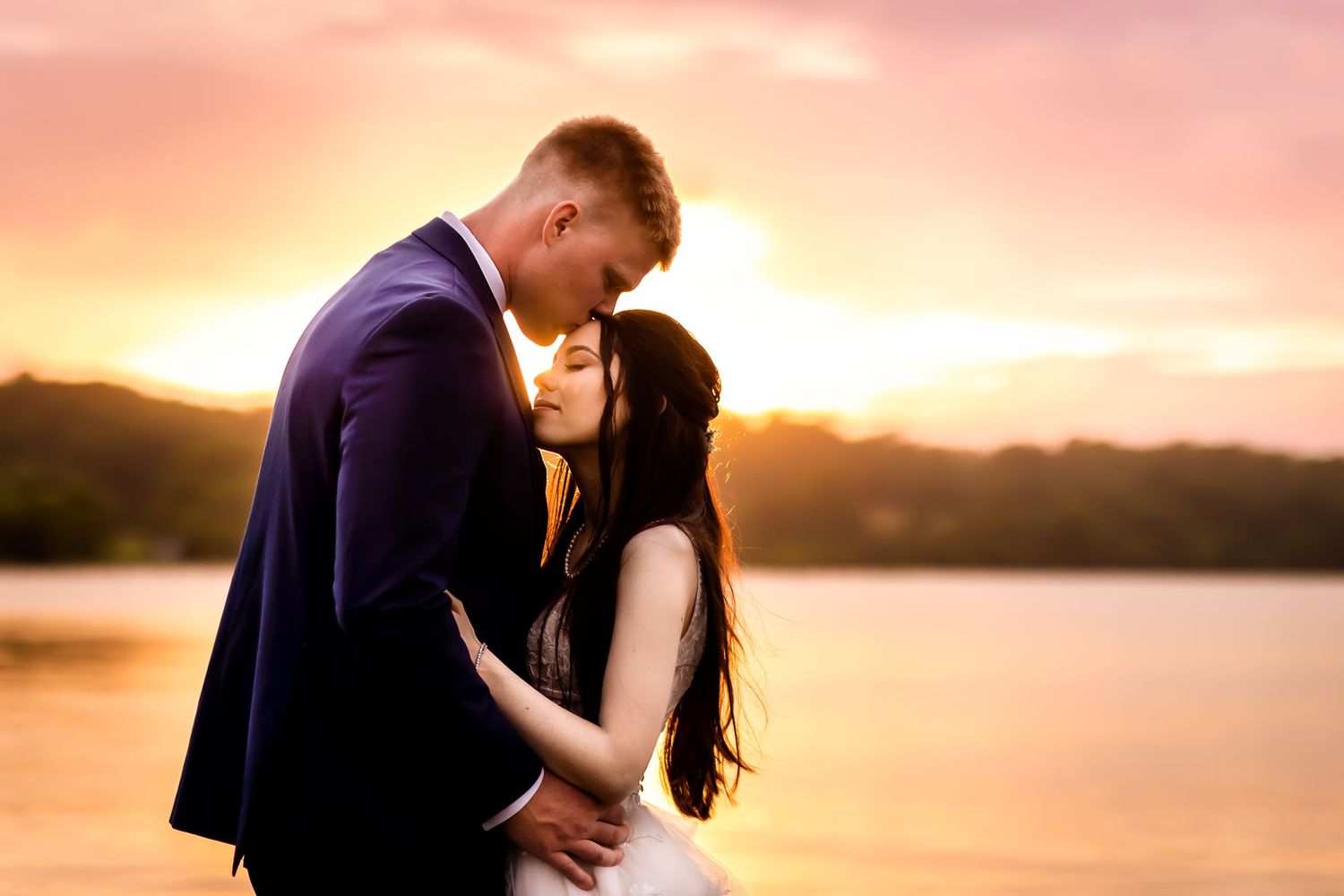 Sunset silhouette of couple sharing romantic moment by lake with orange sky.