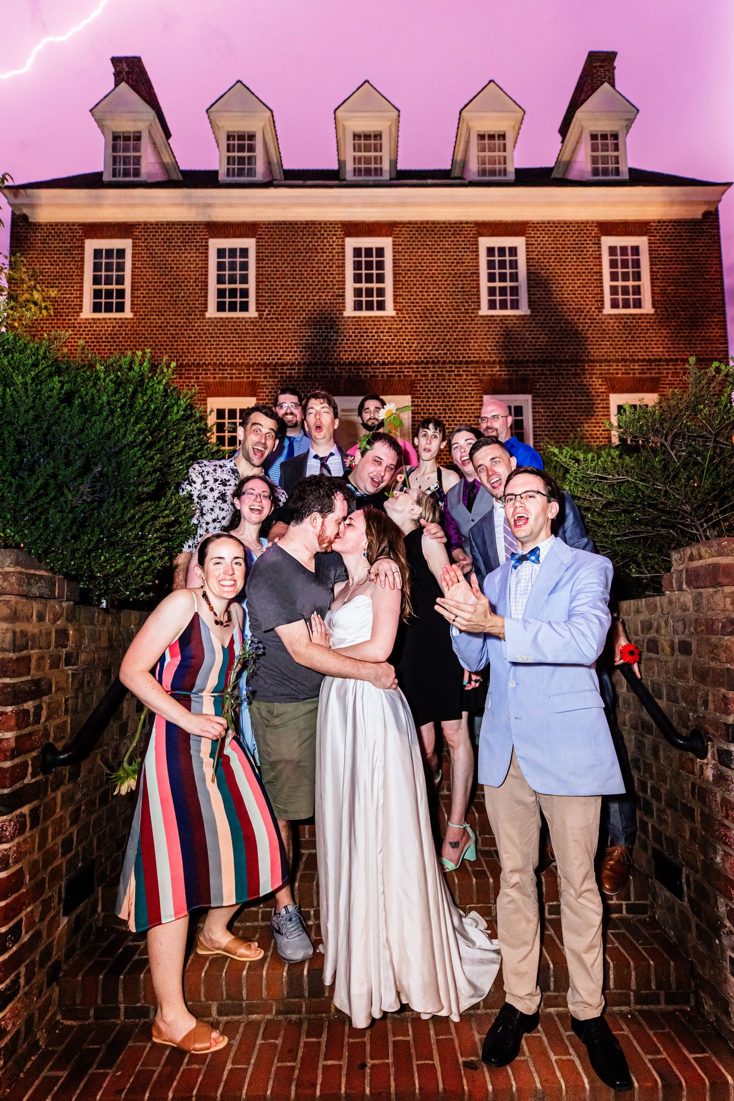Large group poses joyfully on brick steps in front of historic building at sunset.
