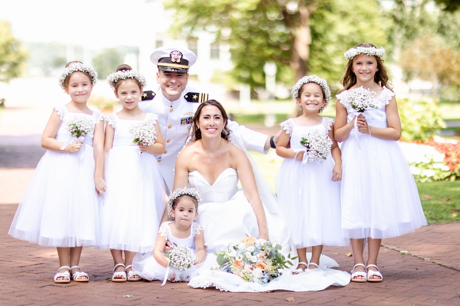 Naval wedding party photo with flower girls in white dresses outdoors.