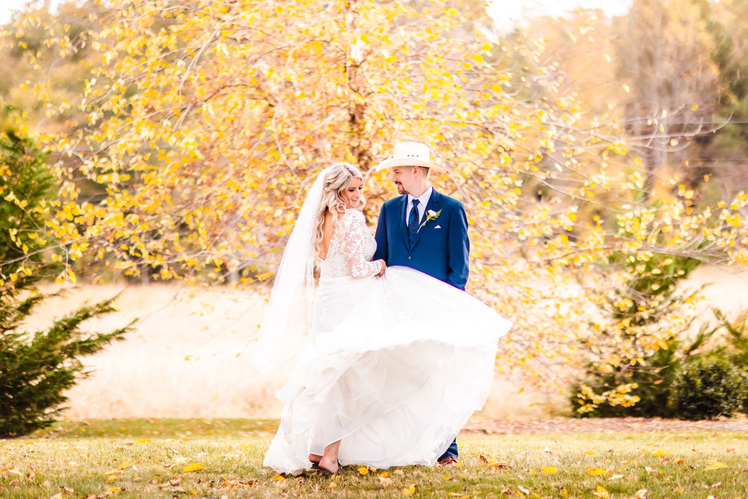 Bride's dress flows in autumn breeze during outdoor wedding portrait session.