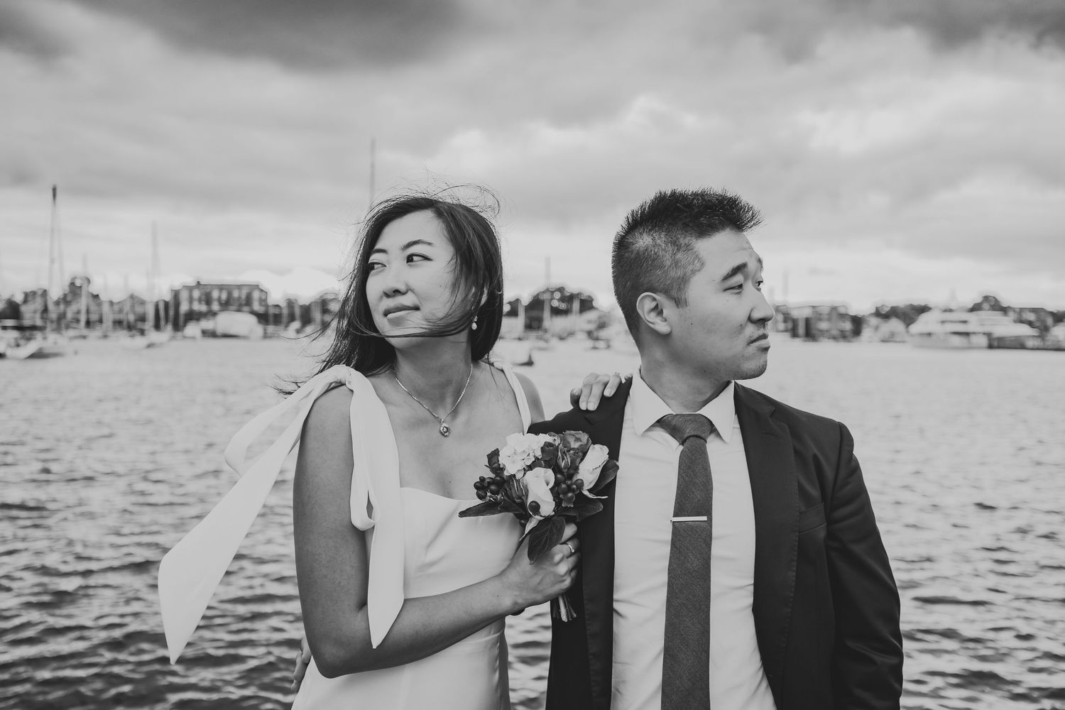 Waterfront wedding portrait with cloudy skies and harbor in background.