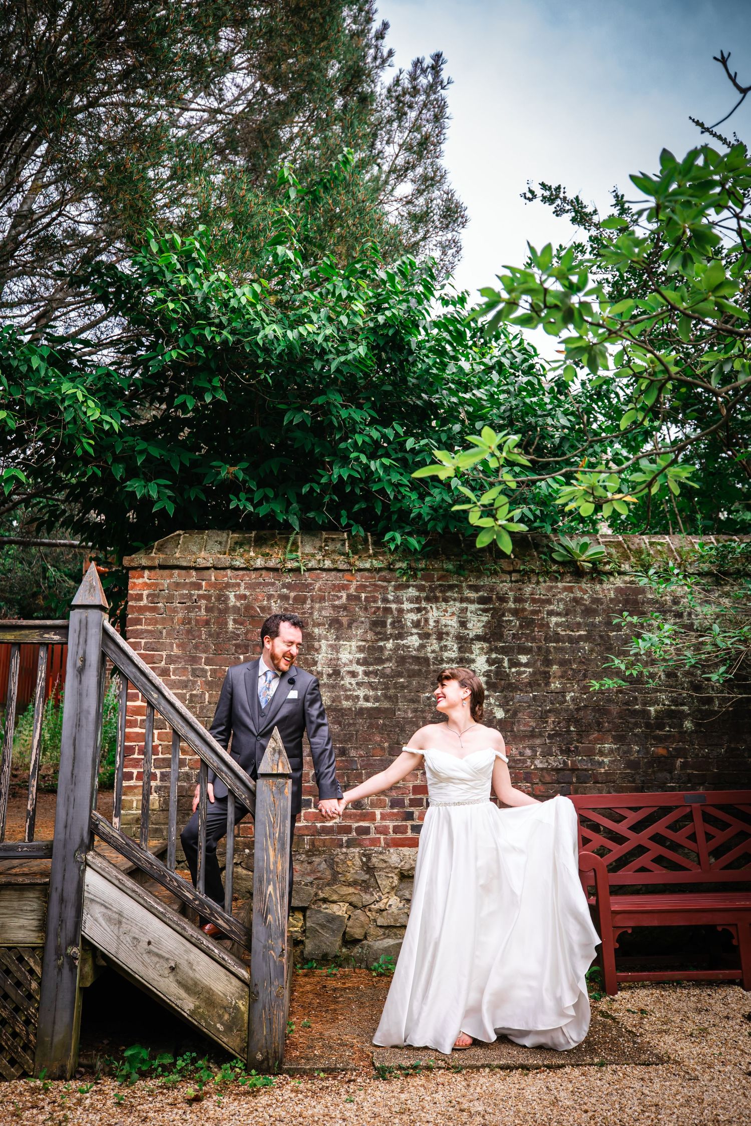 Romantic garden wedding scene with couple on wooden steps against brick wall and lush greenery.