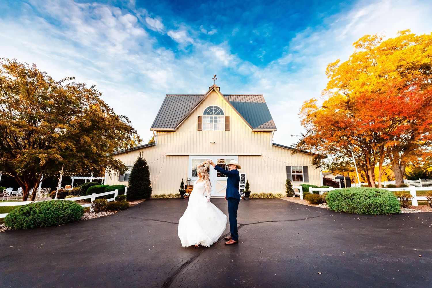 Elegant wedding portrait in front of a white barn venue surrounded by vibrant fall foliage.