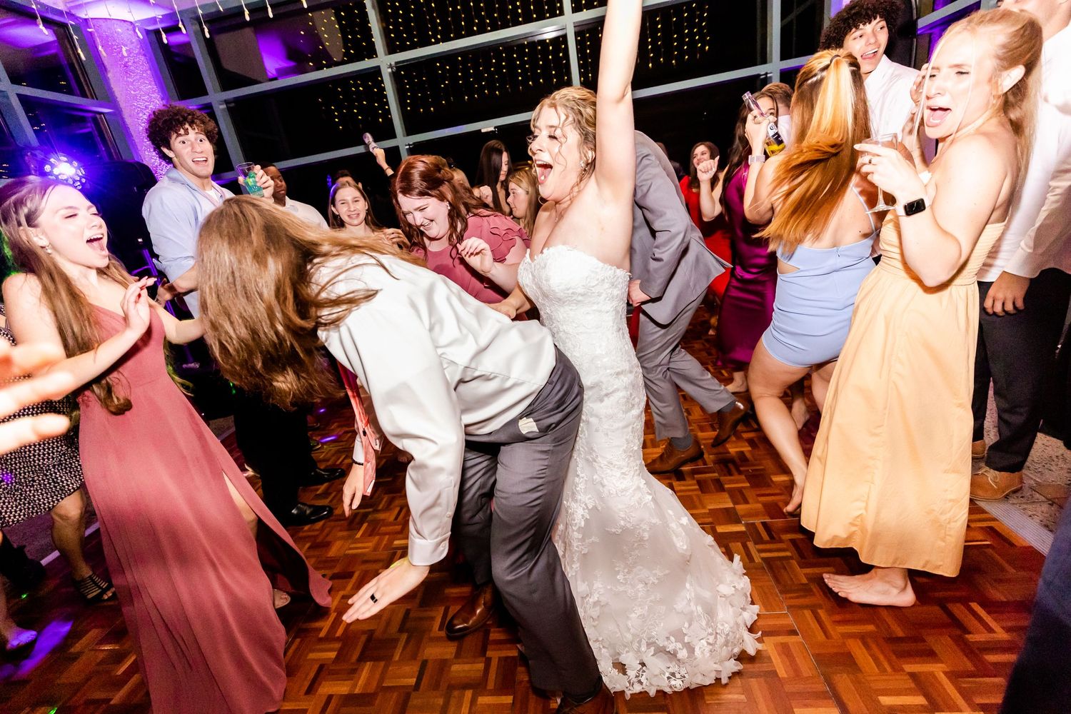 Wedding guests dancing enthusiastically on a wooden dance floor at the reception.