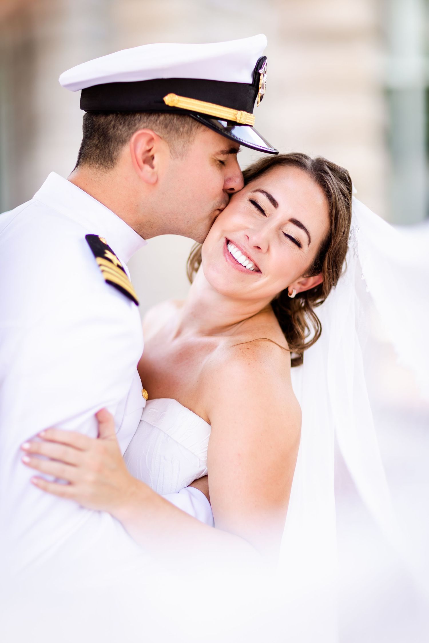 A romantic moment between a bride and naval officer in formal dress uniform sharing a sweet kiss.