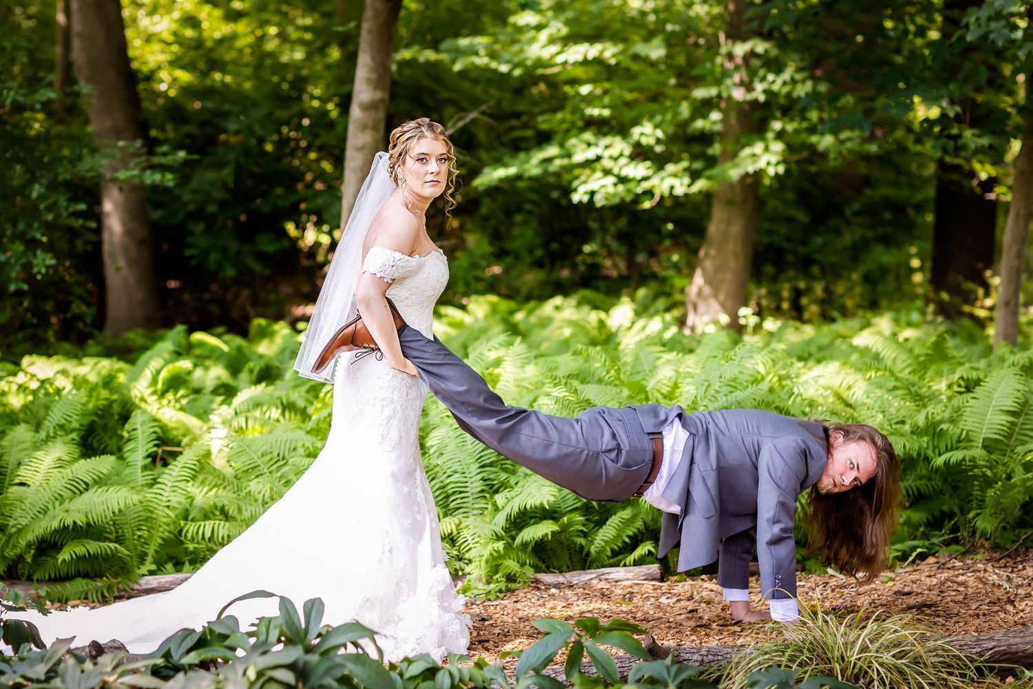 A playful wedding photo in a lush forest setting with ferns and greenery.