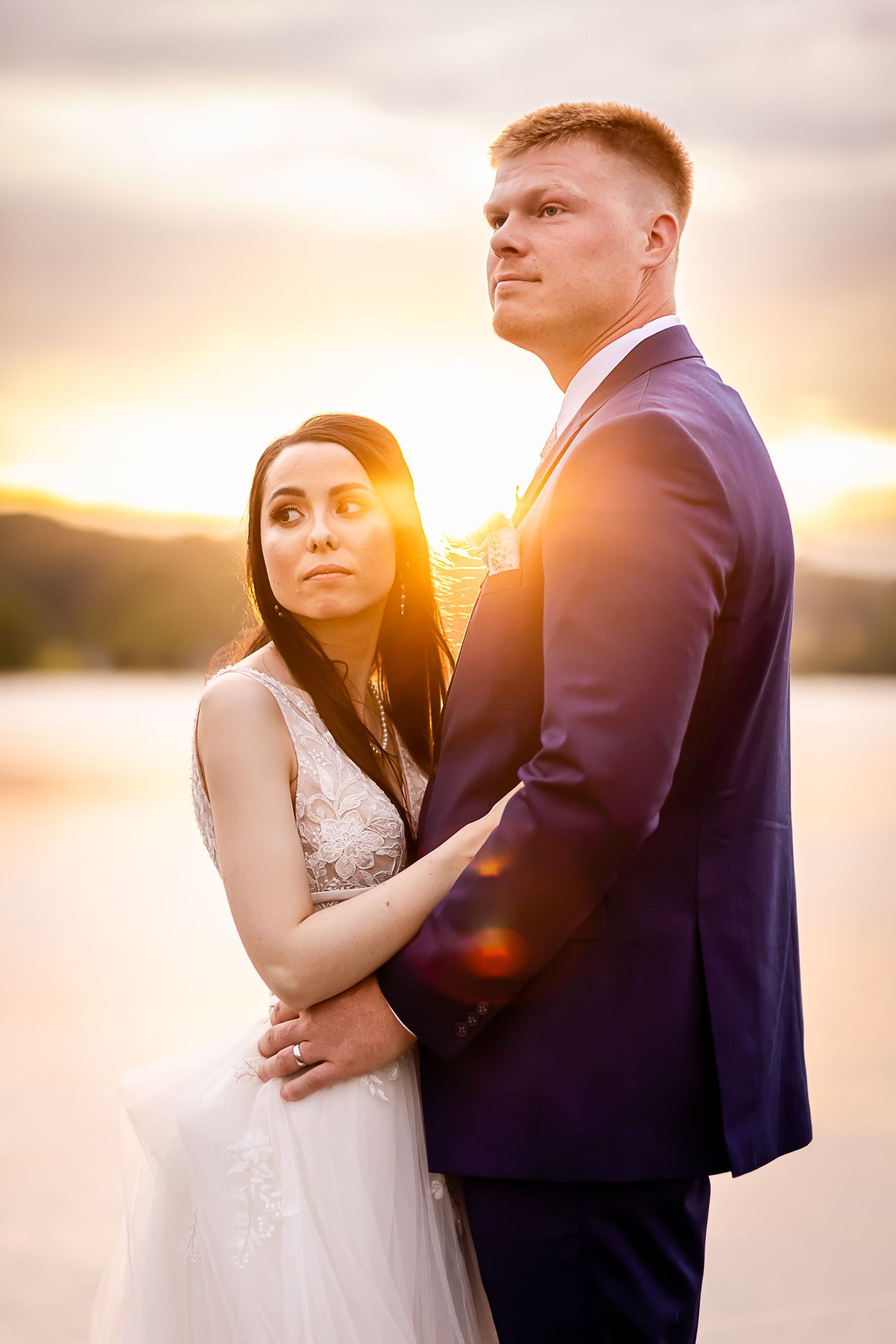 Romantic sunset wedding portrait by water with dramatic golden light.