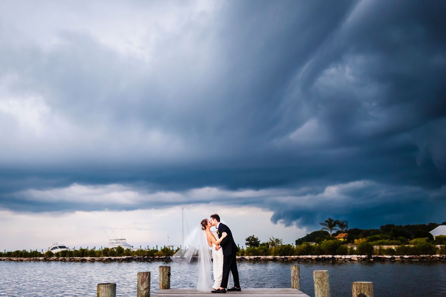 Dramatic stormy sky creates moody backdrop for couple on wooden dock by water.