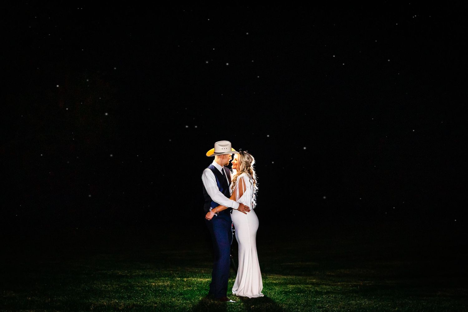 Romantic nighttime wedding portrait of couple under starlit sky.
